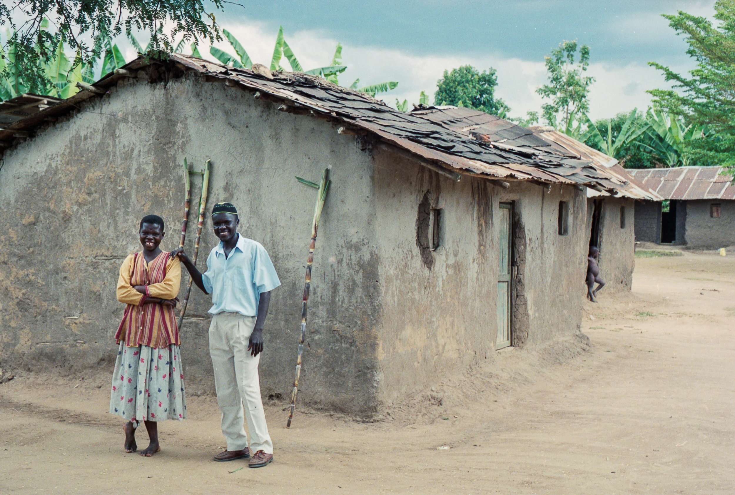 Athaliah Deborah and her husband Musenze Pinehas in front of a typical Eastern Ugandan home. The sugar cane behind them is from a nearby field.
