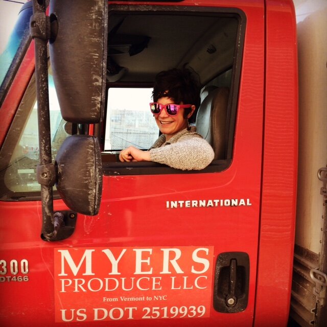  Person sitting in the cab of a truck with arm out the window and sunglasses on . 