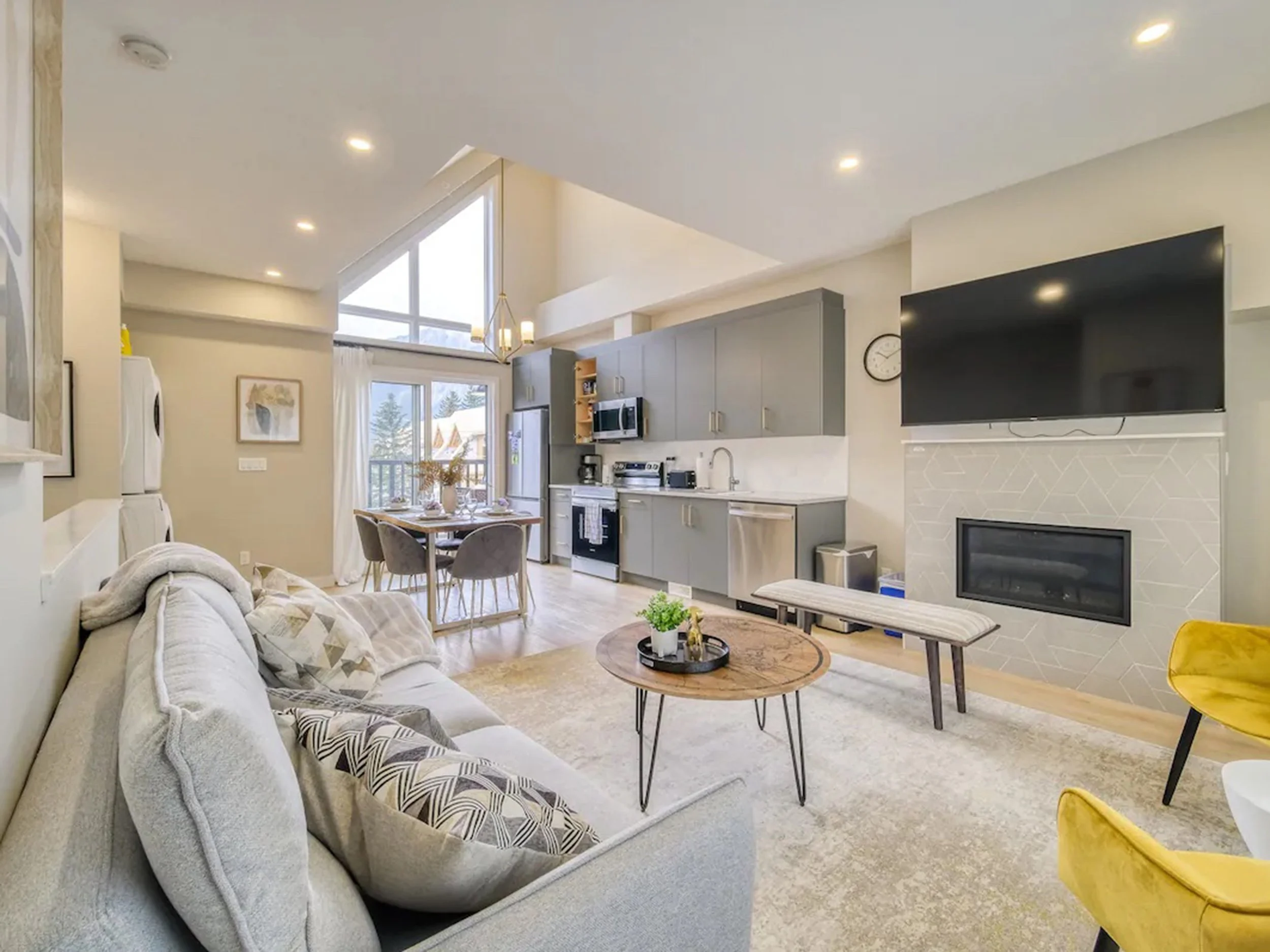 Modern open-concept living room and kitchen with high ceilings, large window, and contemporary furniture.