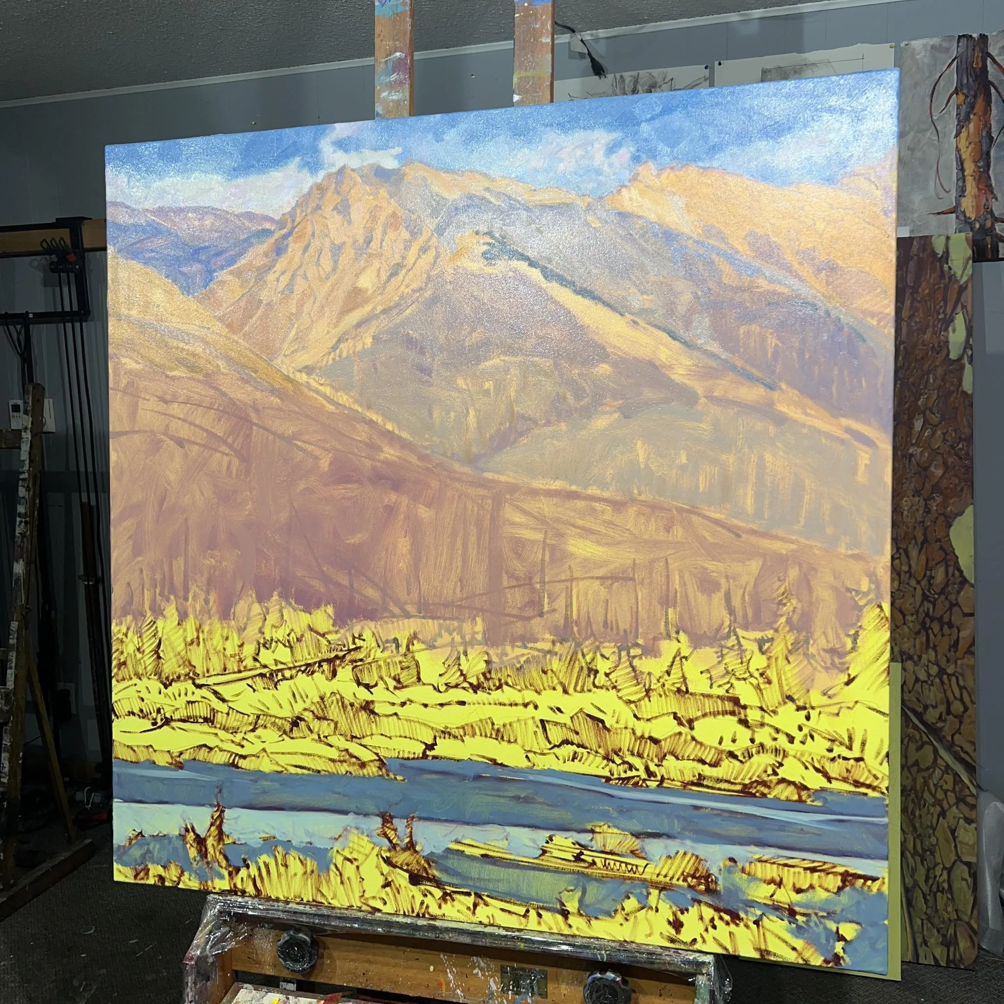 A landscape painting of a mountain range with yellow fields and a river in the foreground.
