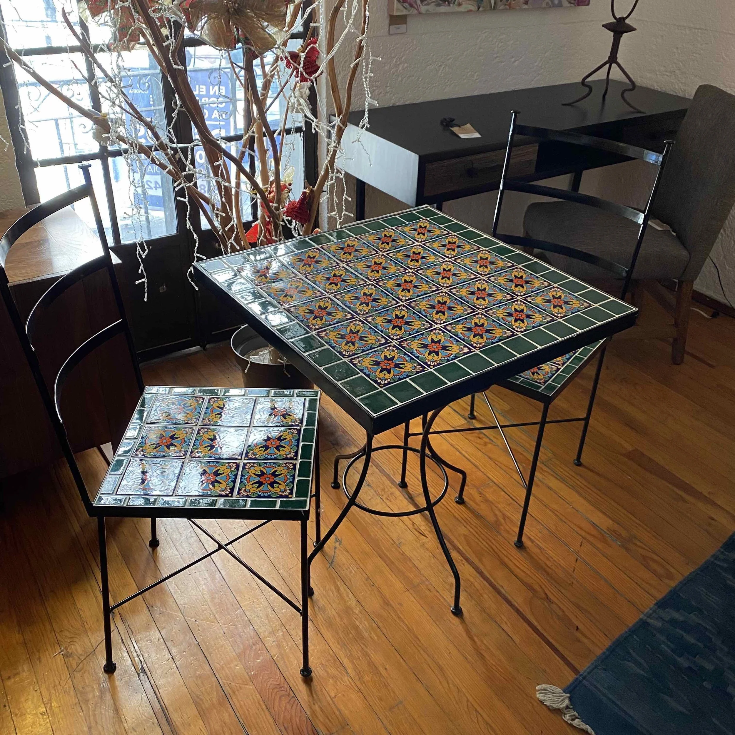 Mesa y silla con azulejos decorativos en interior de restaurante, con florero y ventana de fondo.