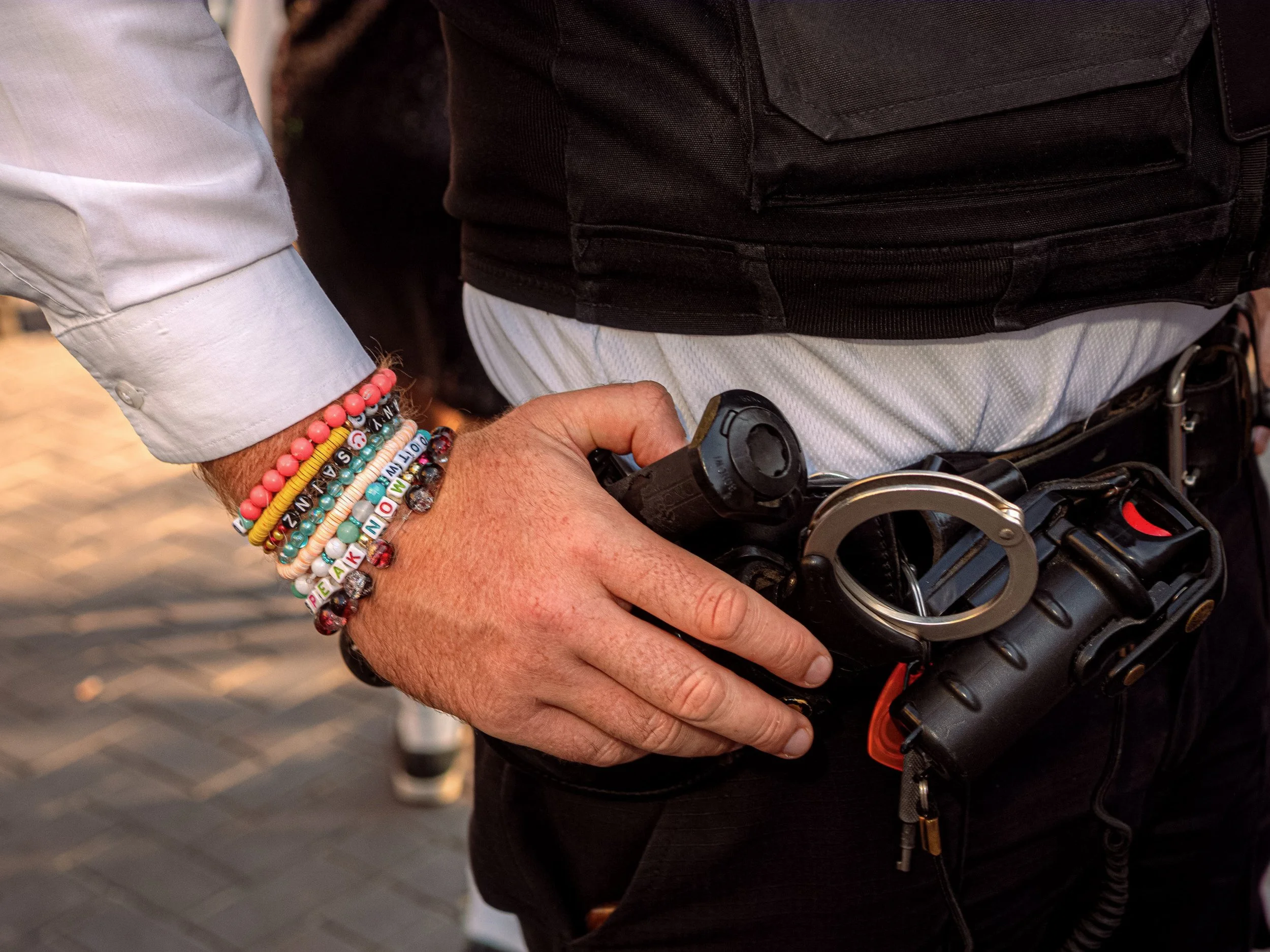 Close-up of a police officer’s wrist covered in friendship bracelets beside handcuffs and equipment on a belt.