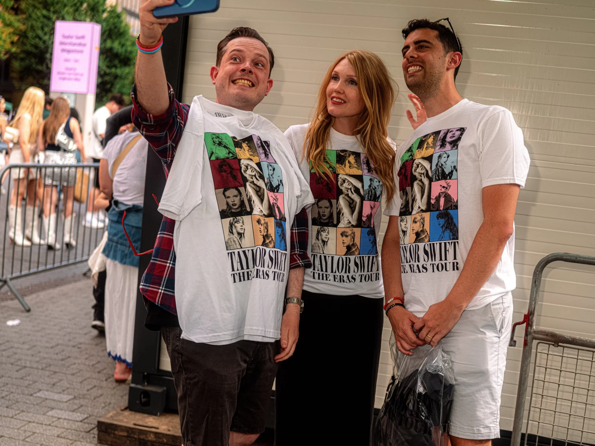 Three Taylor Swift fans in matching Eras Tour T-shirts pose together for a phone selfie.