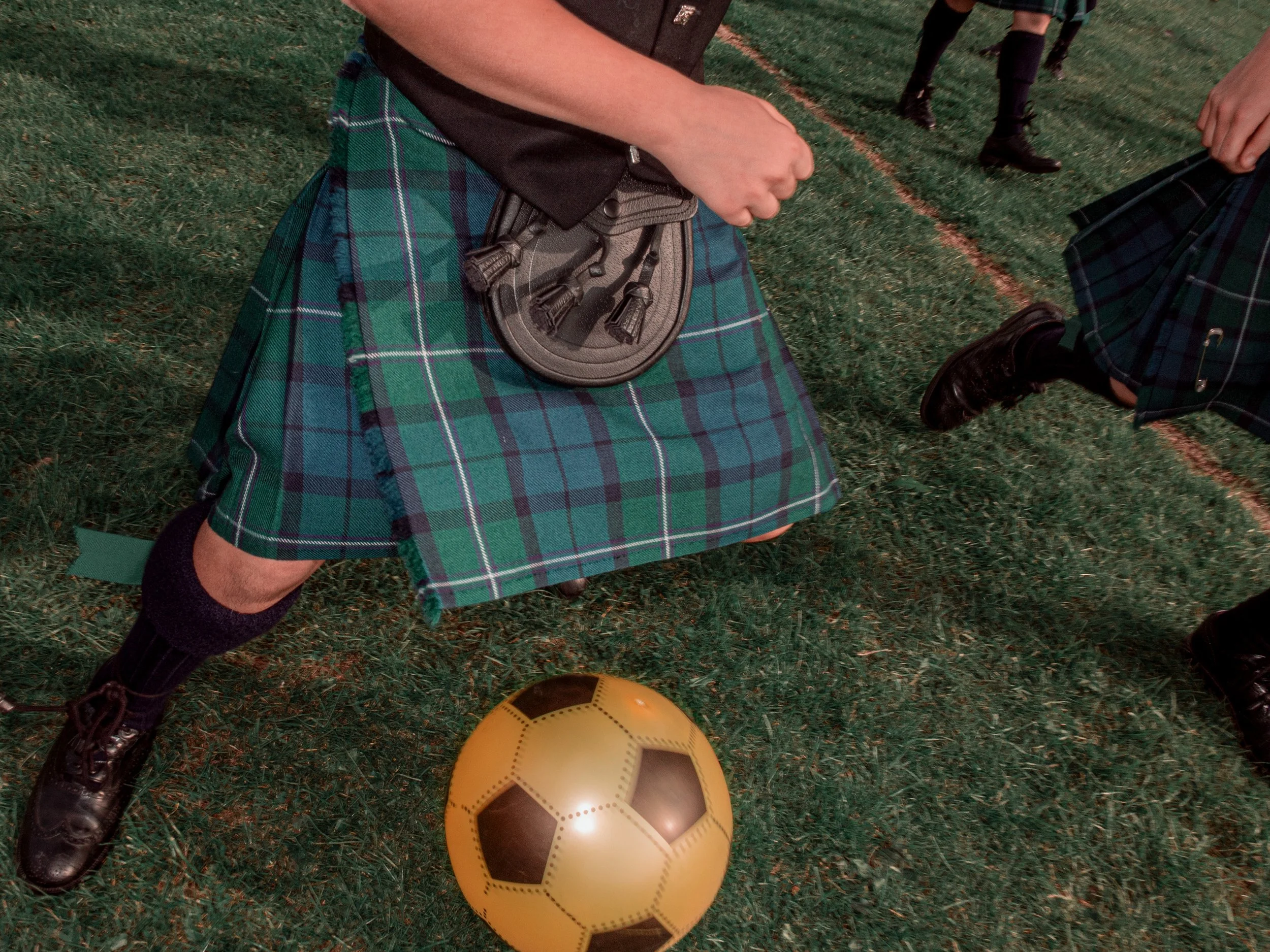 A man in a kilt and sporran stands over a football on the grass.