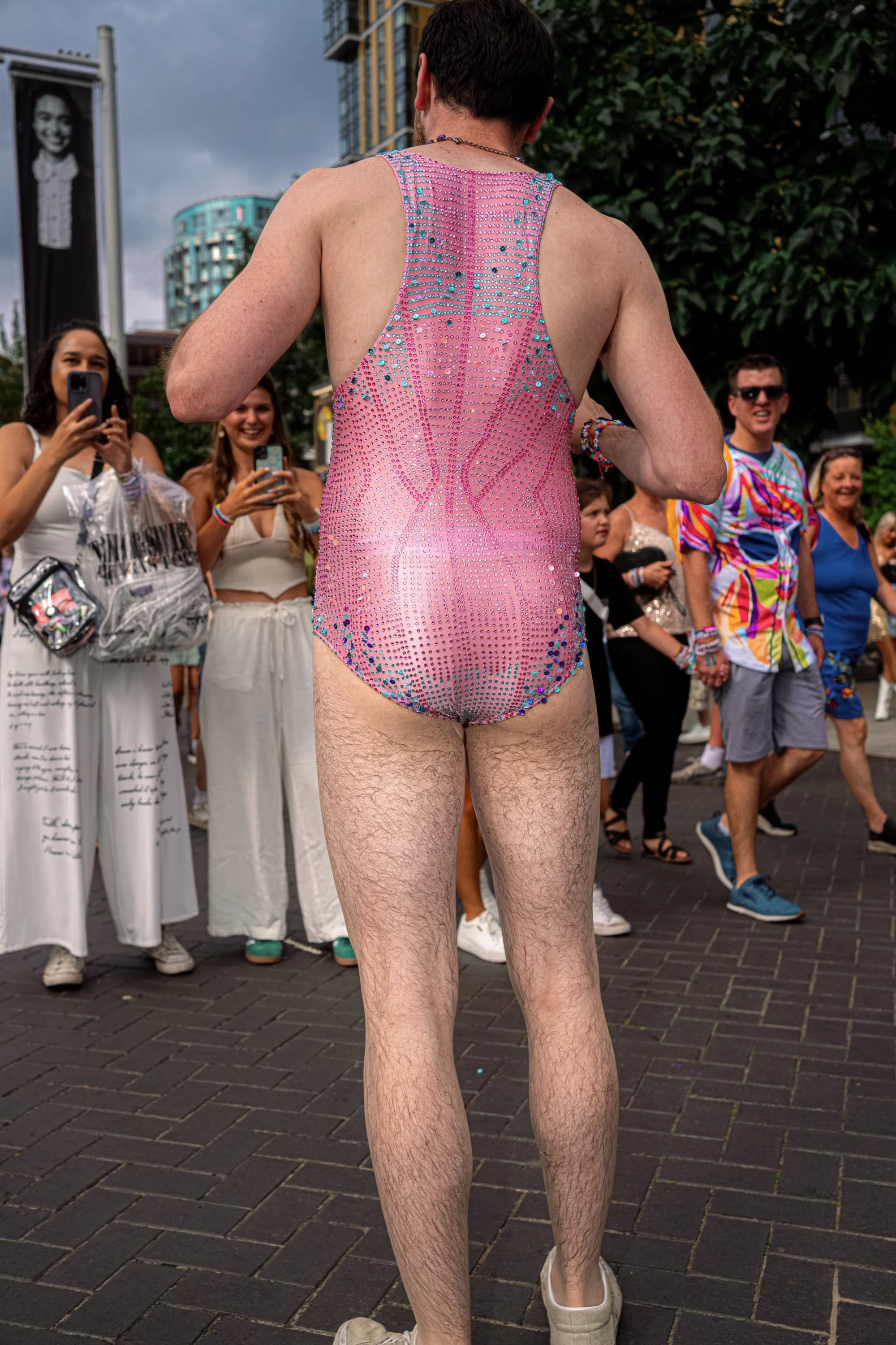 A Taylor Swift fan in a pink sequinned bodysuit poses with their back to the camera as other fans take photographs.