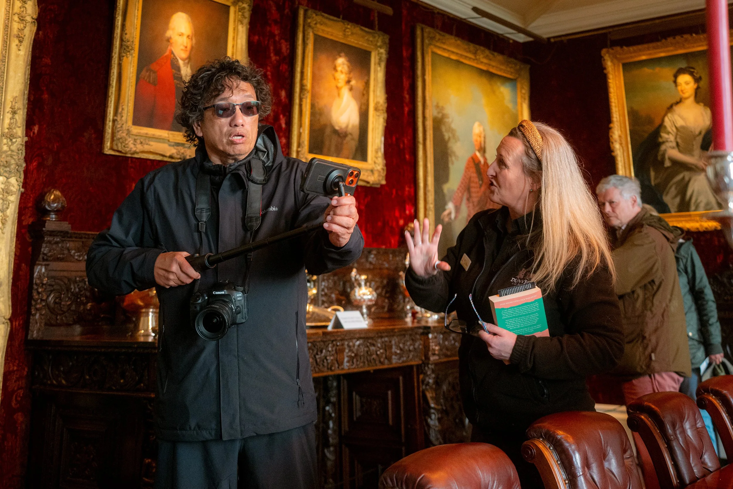 At Dunvegan Castle, a visitor films on a selfie stick in a red-walled room hung with portraits.