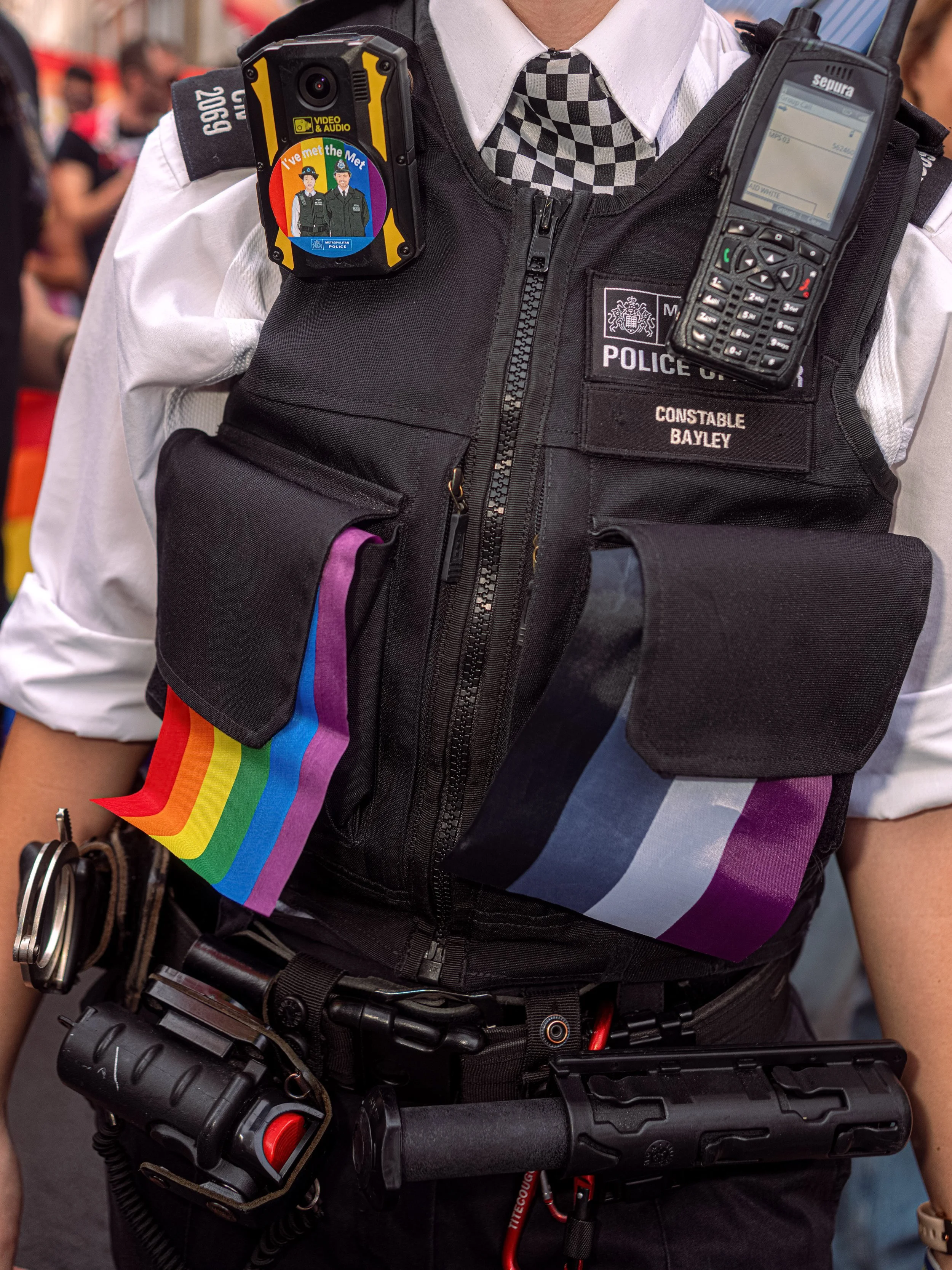 Close-up of a police officer’s equipment vest decorated with rainbow flags.