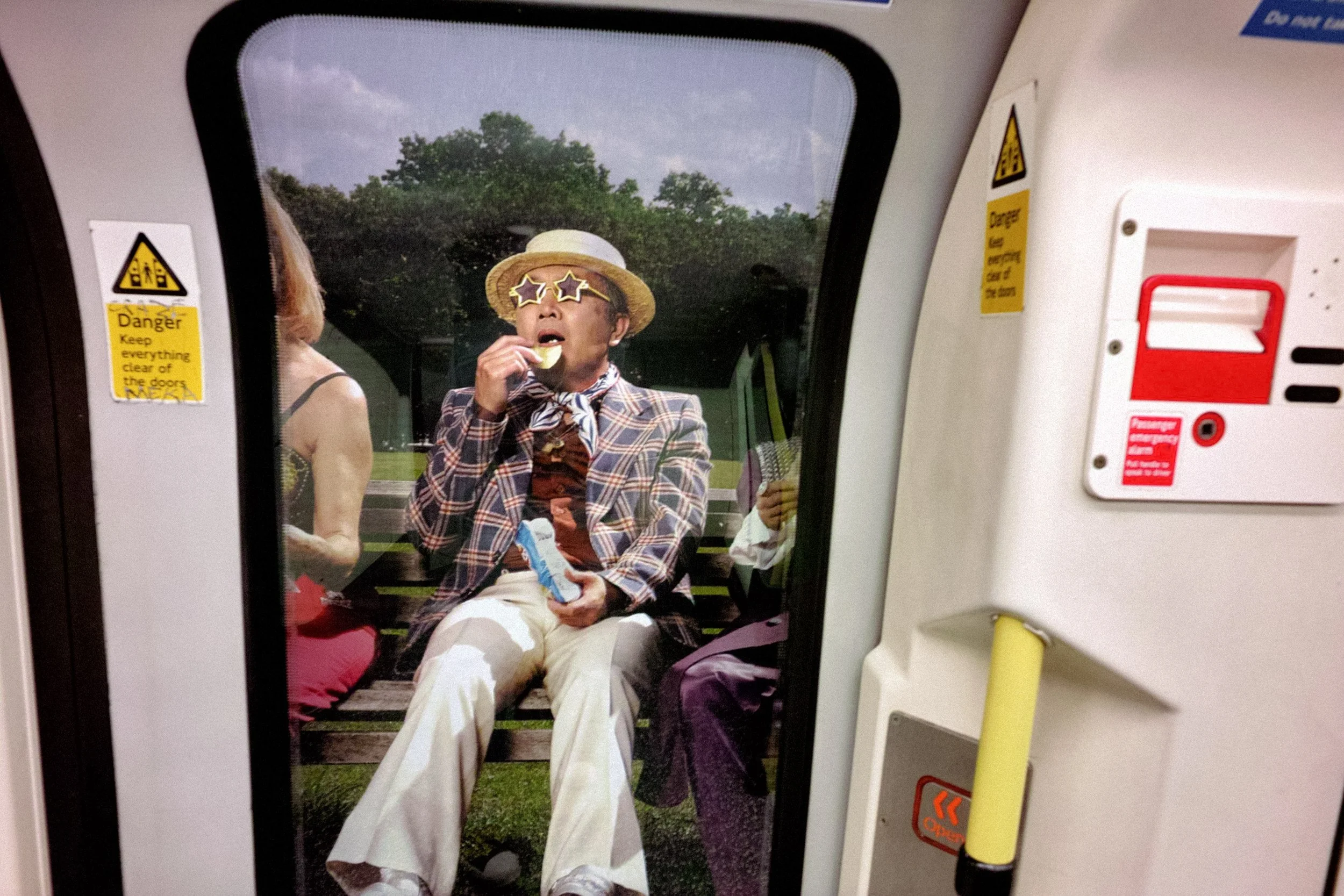 A passenger in a straw hat eats a snack beside the door of a train.
