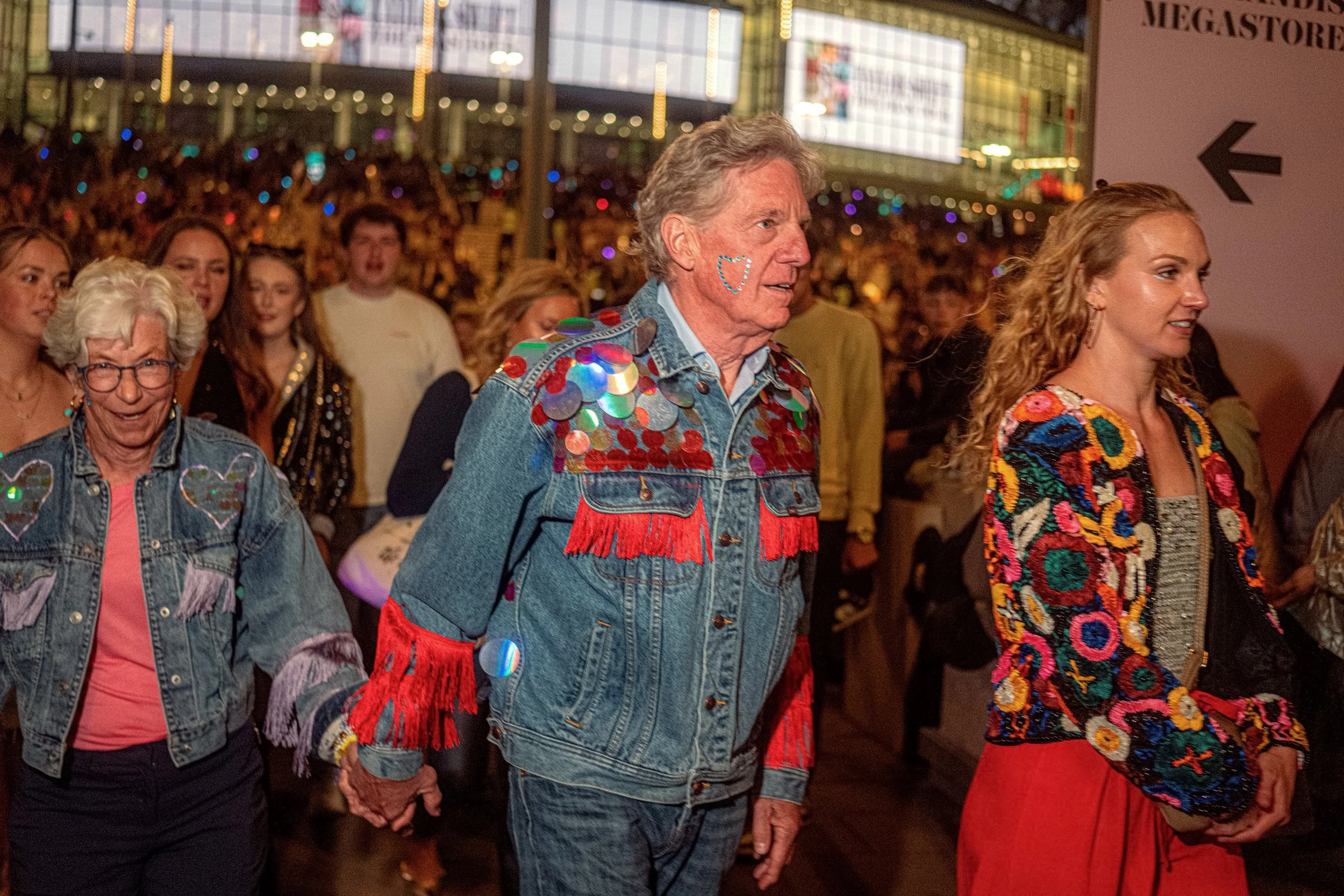 Taylor Swift fans walk through a crowded concourse in brightly decorated denim jackets.