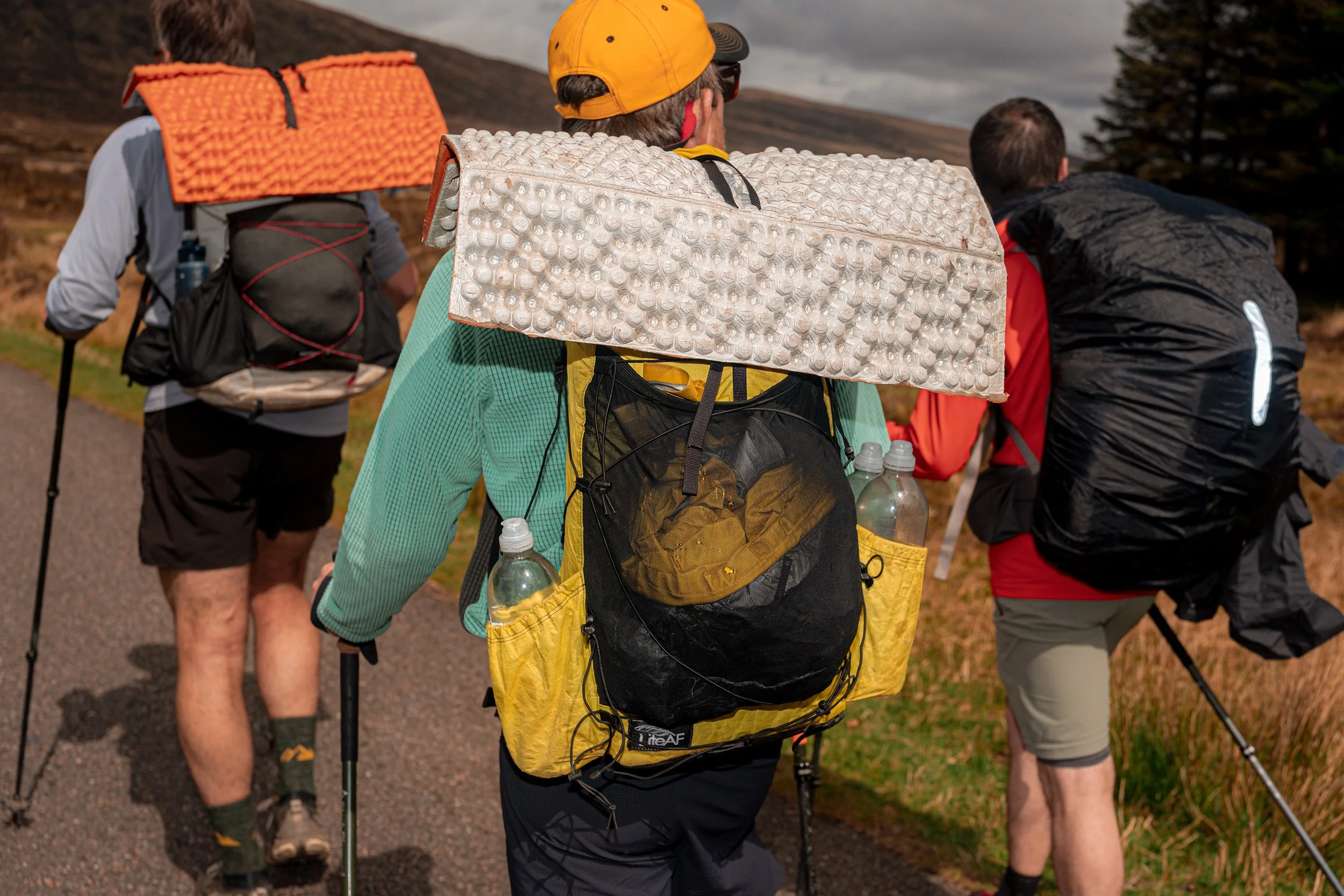 Walkers with big rucksacks and sleeping mats set off along a hill path.