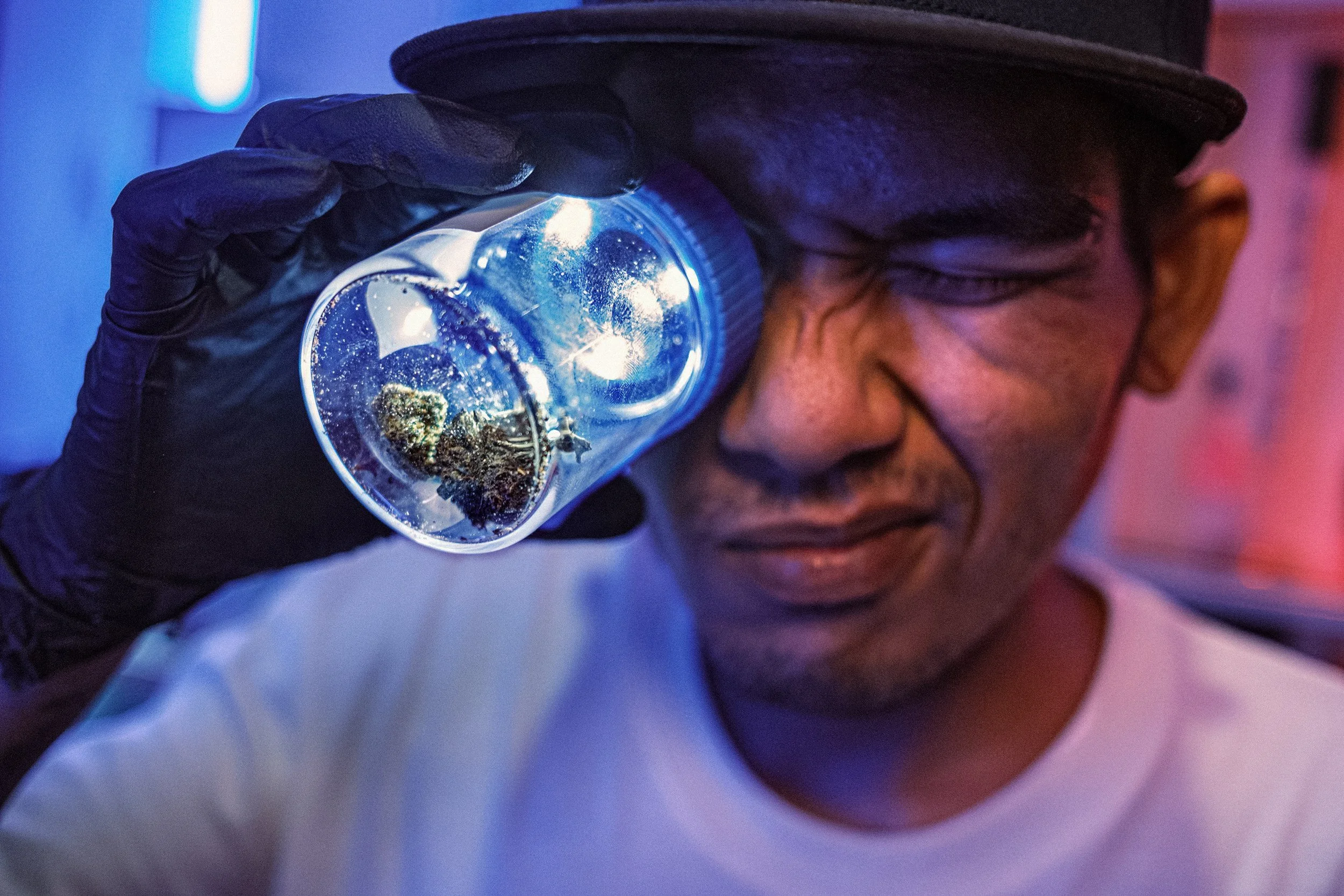 A person holds an illuminated magnifying jar containing cannabis buds to one eye in a shop in Thailand.
