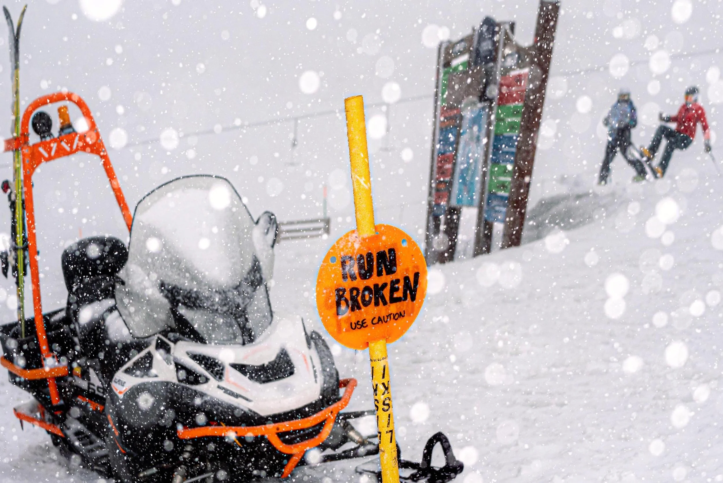 A snowmobile stands beside a Run Broken sign as snow falls and skiers pass behind.
