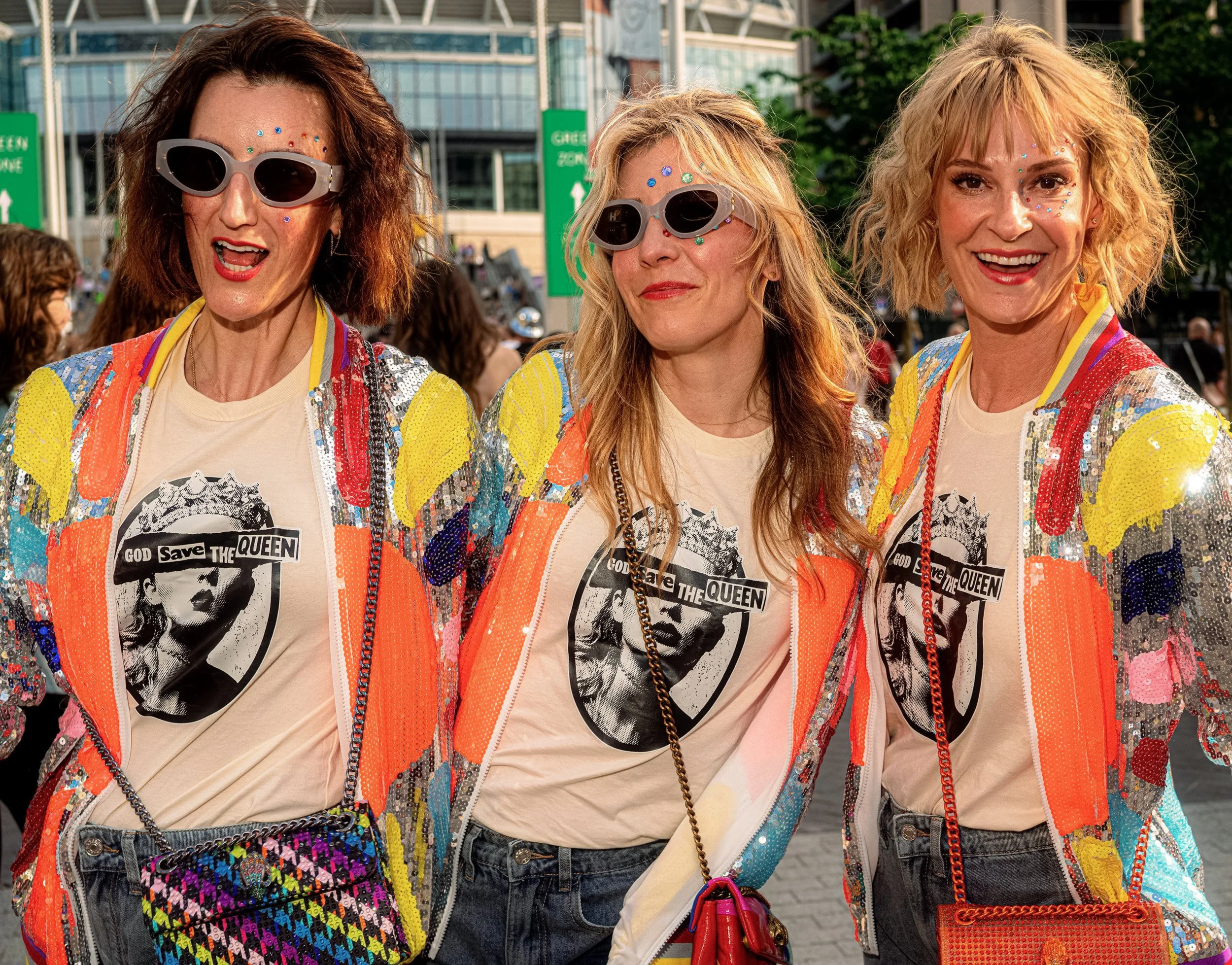 Three Taylor Swift fans wear matching multicoloured sequinned jackets, graphic T-shirts and small oval sunglasses.