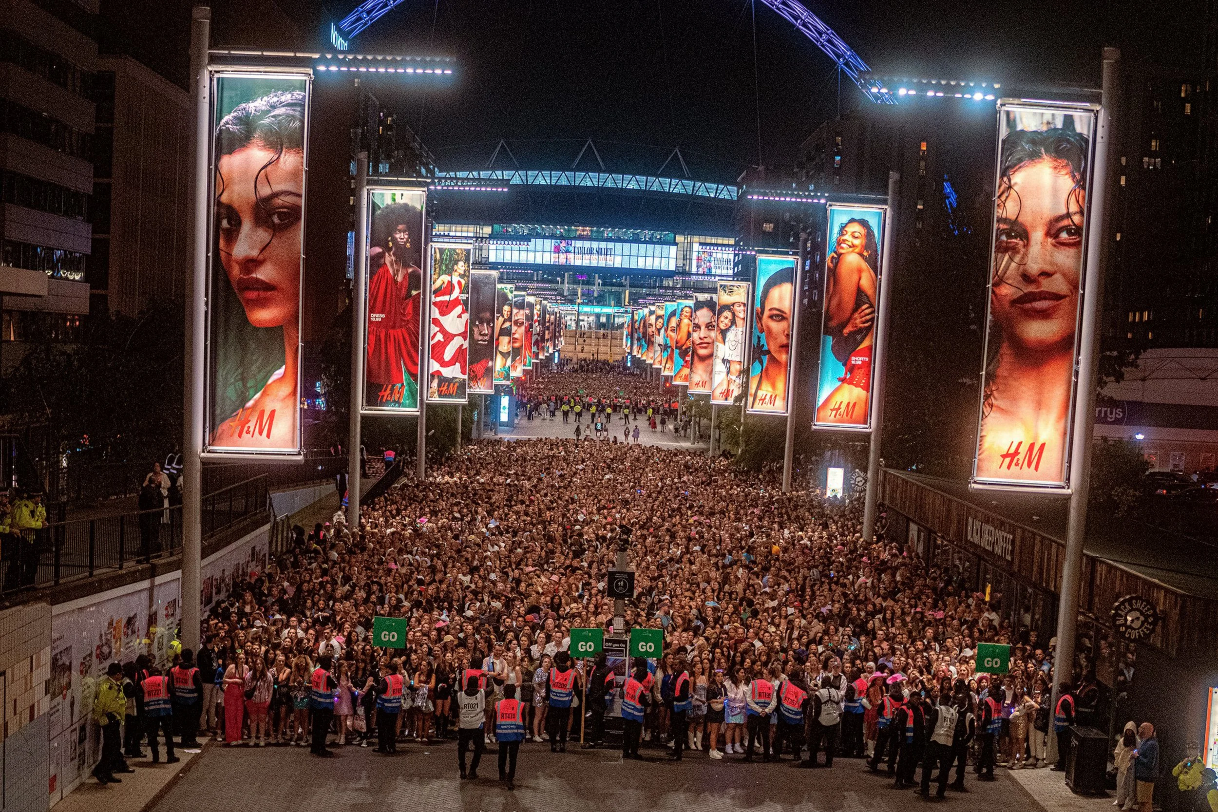 A huge crowd fills the illuminated walkway outside Wembley Stadium at night after the Taylor Swift concert.