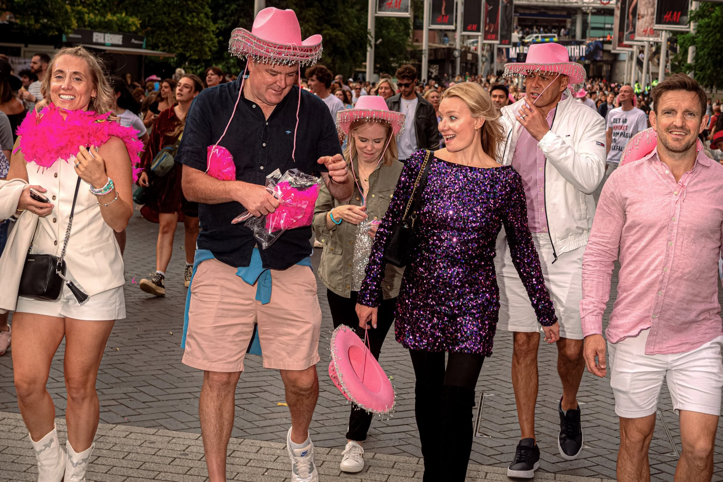 Taylor Swift fans in pink cowboy hats walk towards the concert carrying pink feather boas.