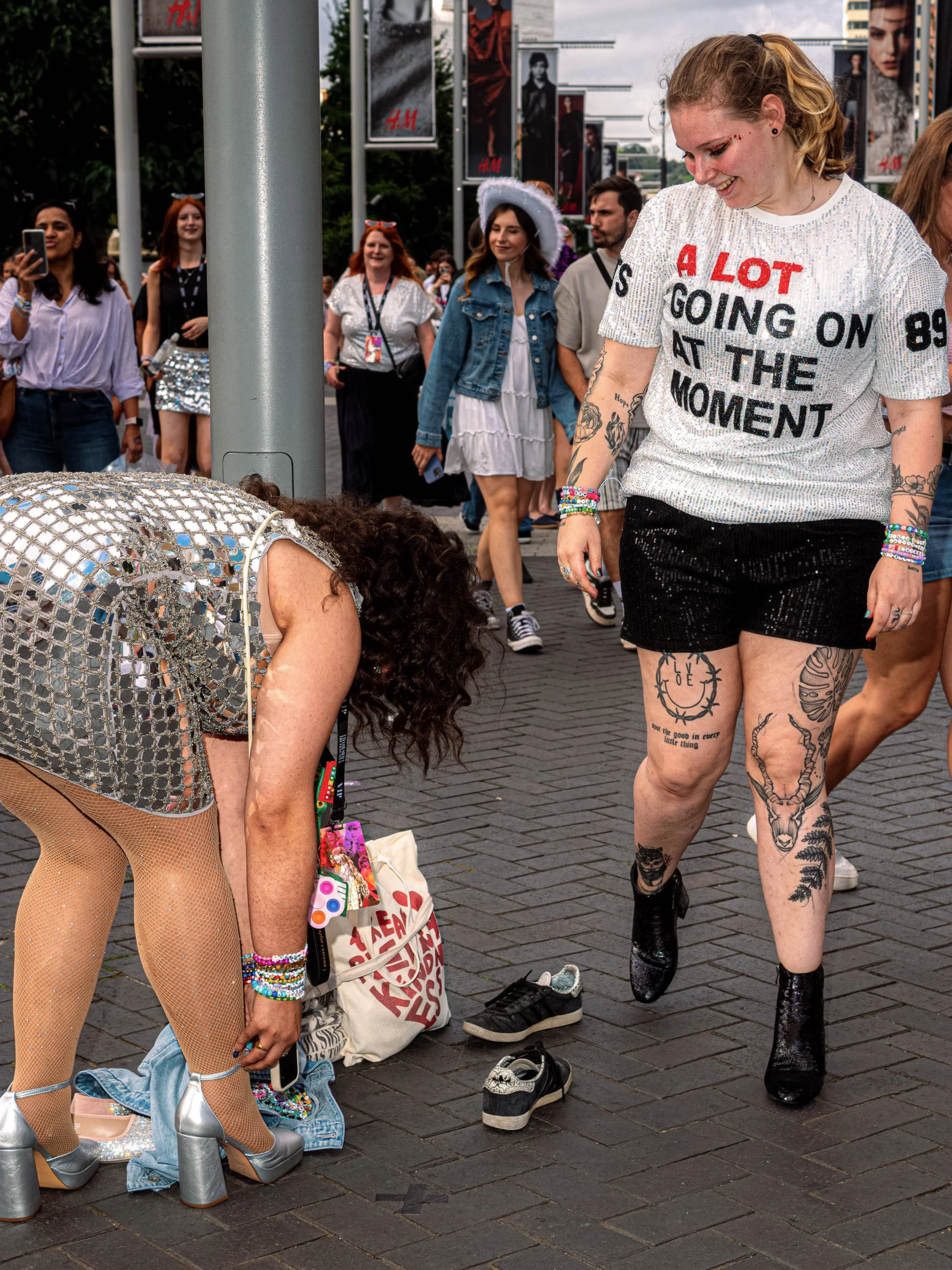Taylor Swift fans change footwear on the pavement, with trainers and cowboy boots beside them.