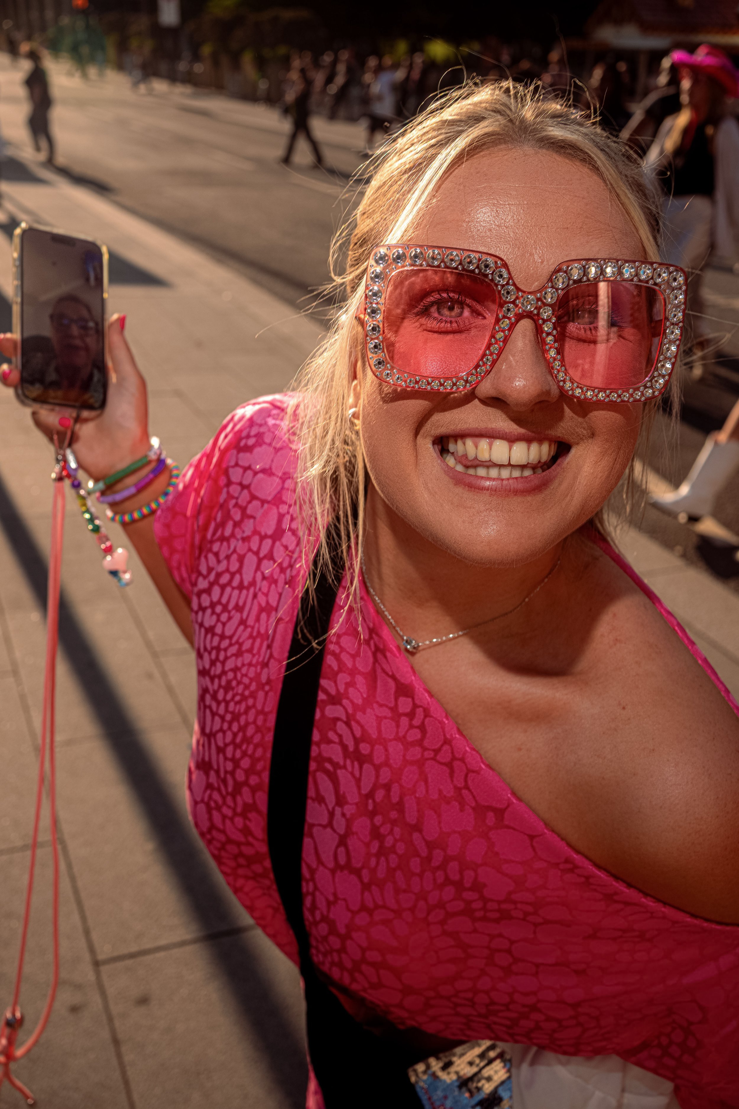A smiling Taylor Swift fan in a bright pink top wears oversized pink sunglasses decorated with beads.