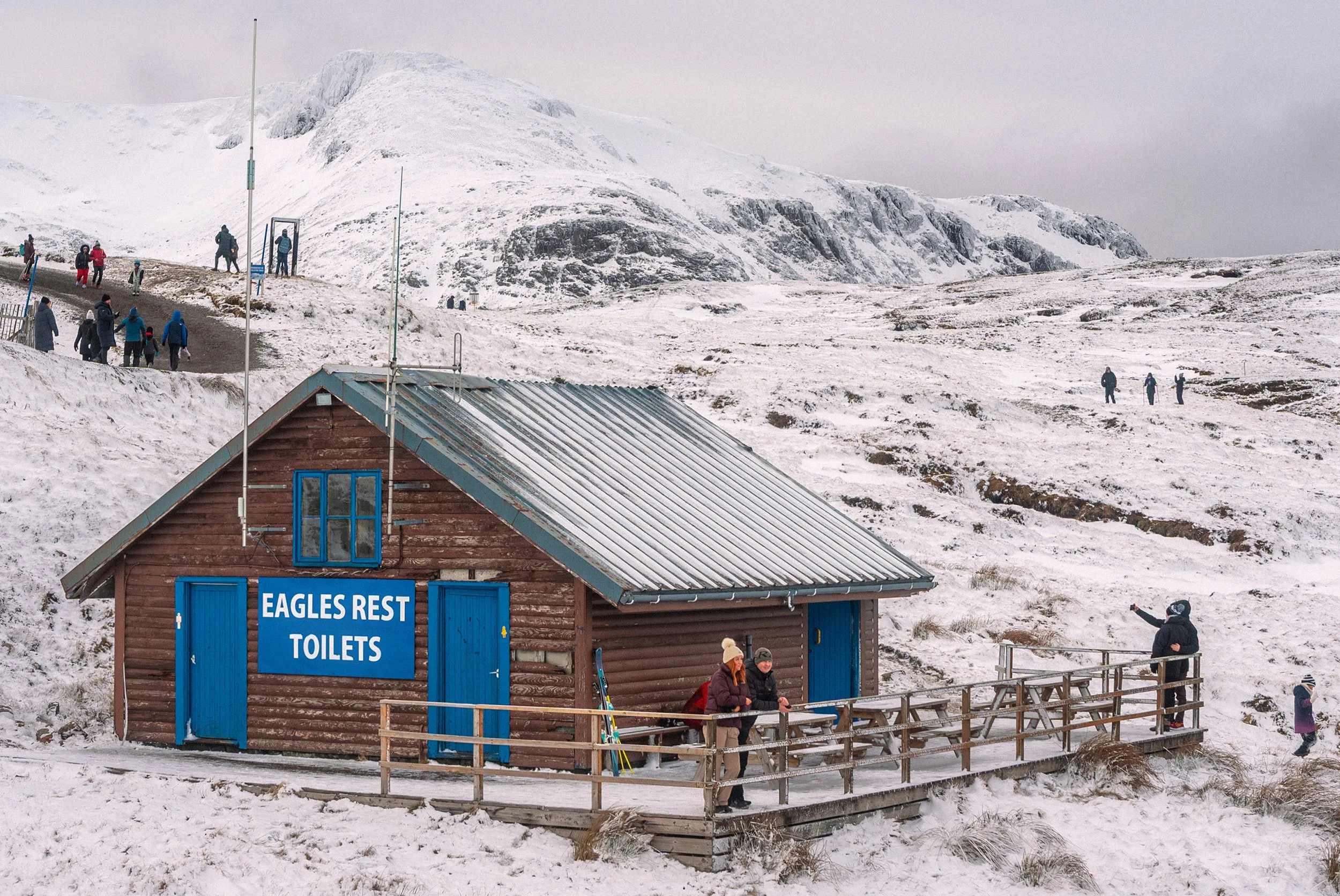 Walkers gather by the Eagles Rest toilets hut on a snowy hillside.