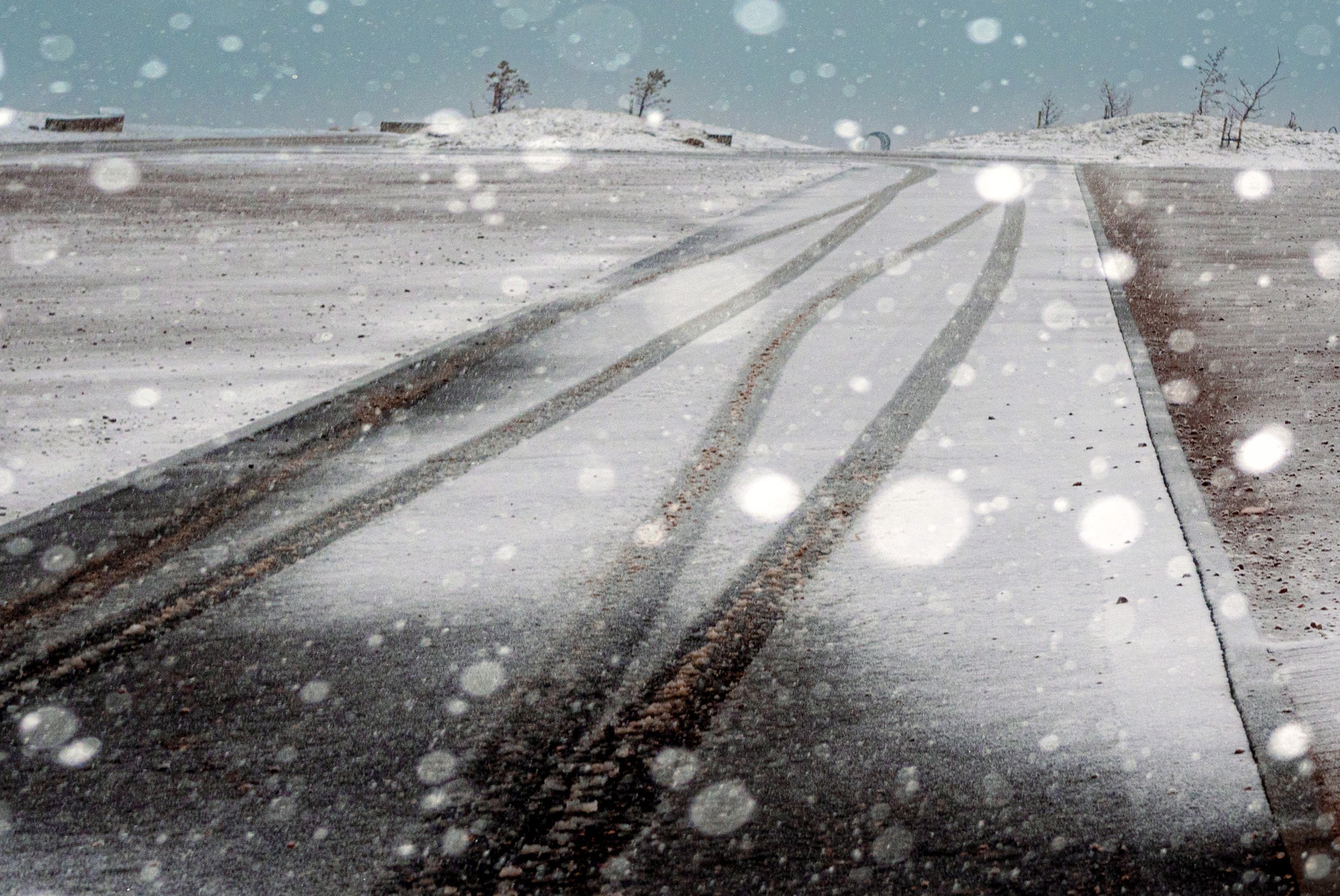 Tyre tracks run through fresh snow on an empty road as snow falls.