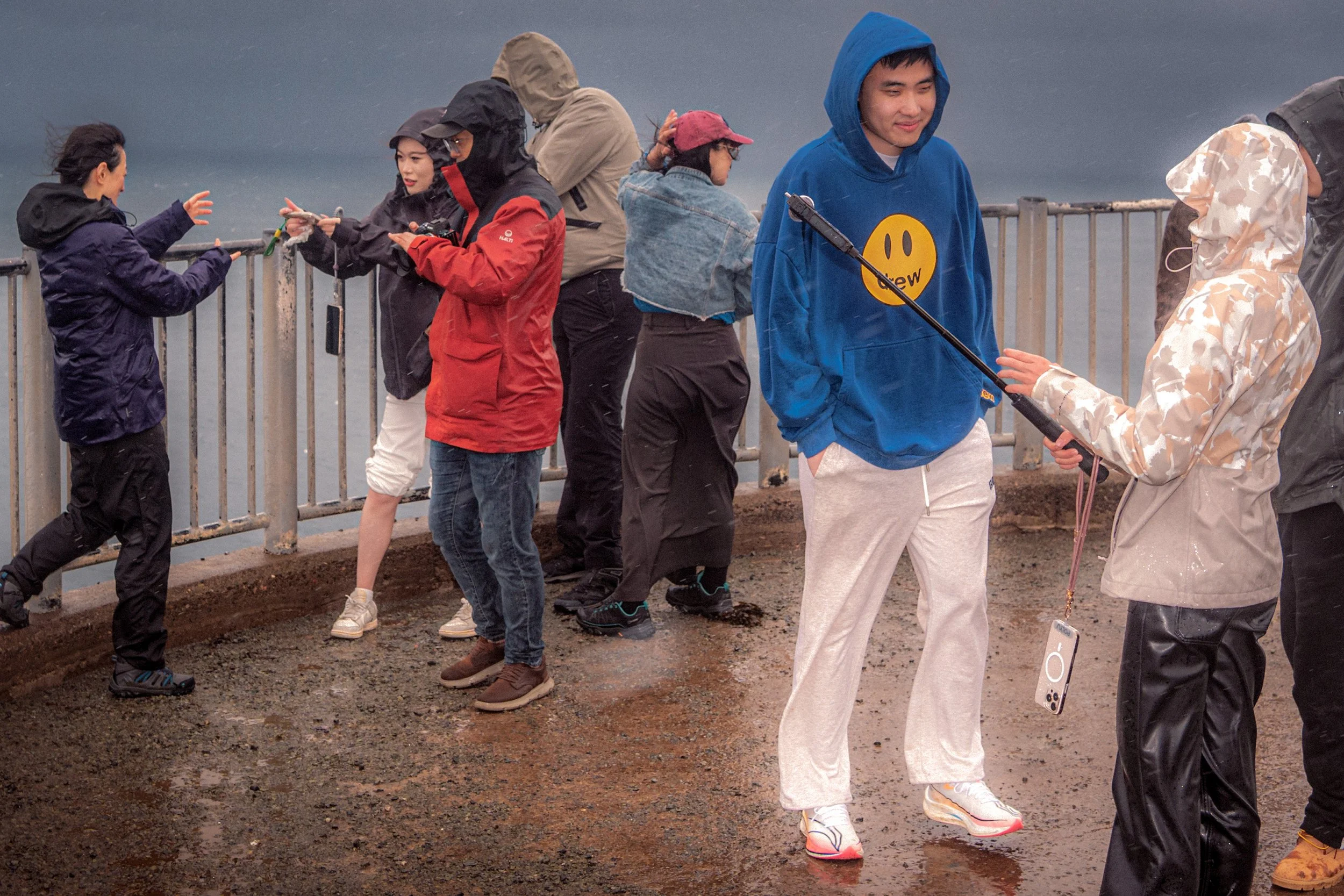 Visitors in hoods and rain jackets film and take photographs on a wet, windy viewing platform.