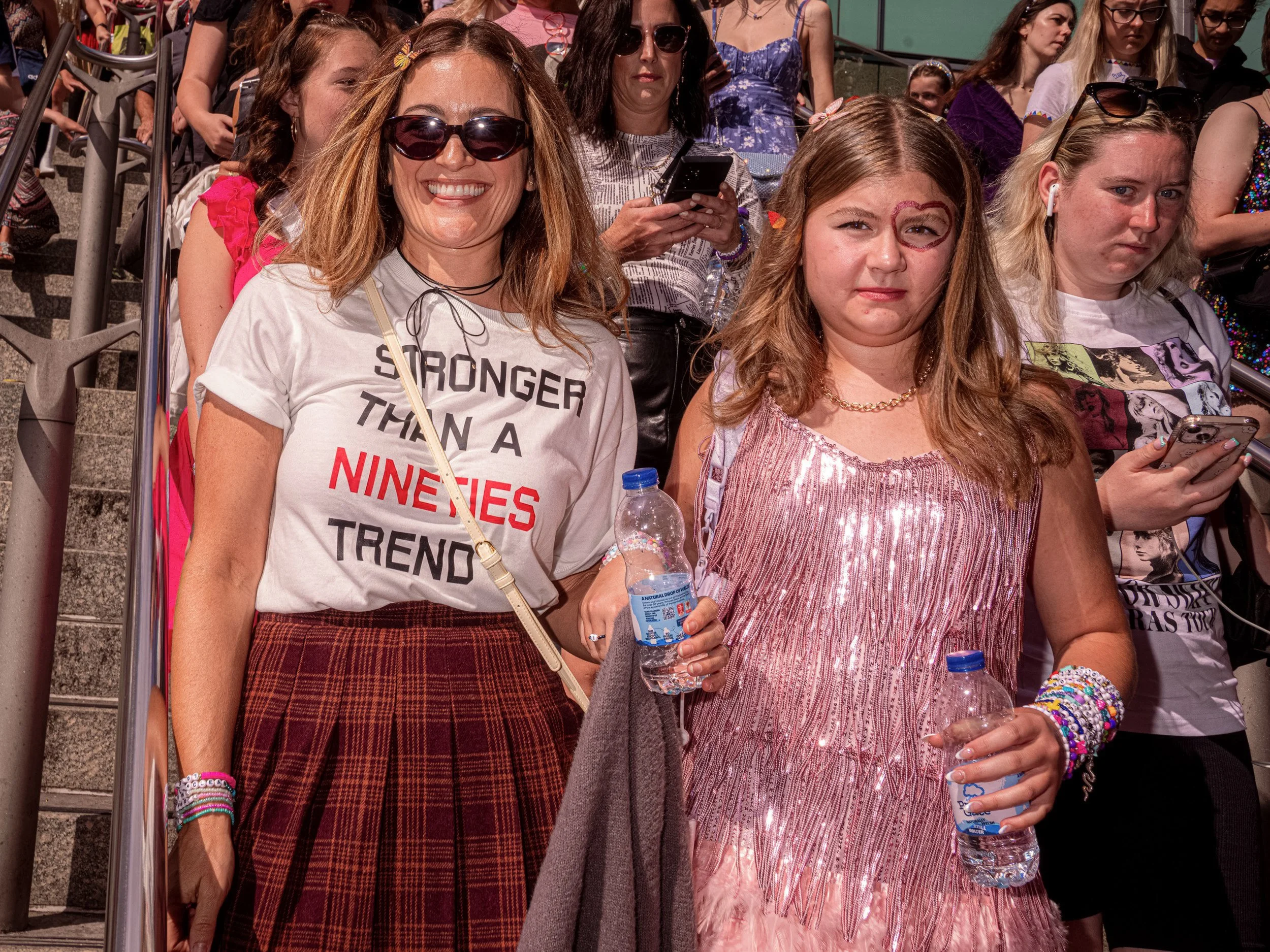 Two Taylor Swift fans descend steps, one in a slogan T-shirt and tartan skirt, the other in a pink fringed dress.
