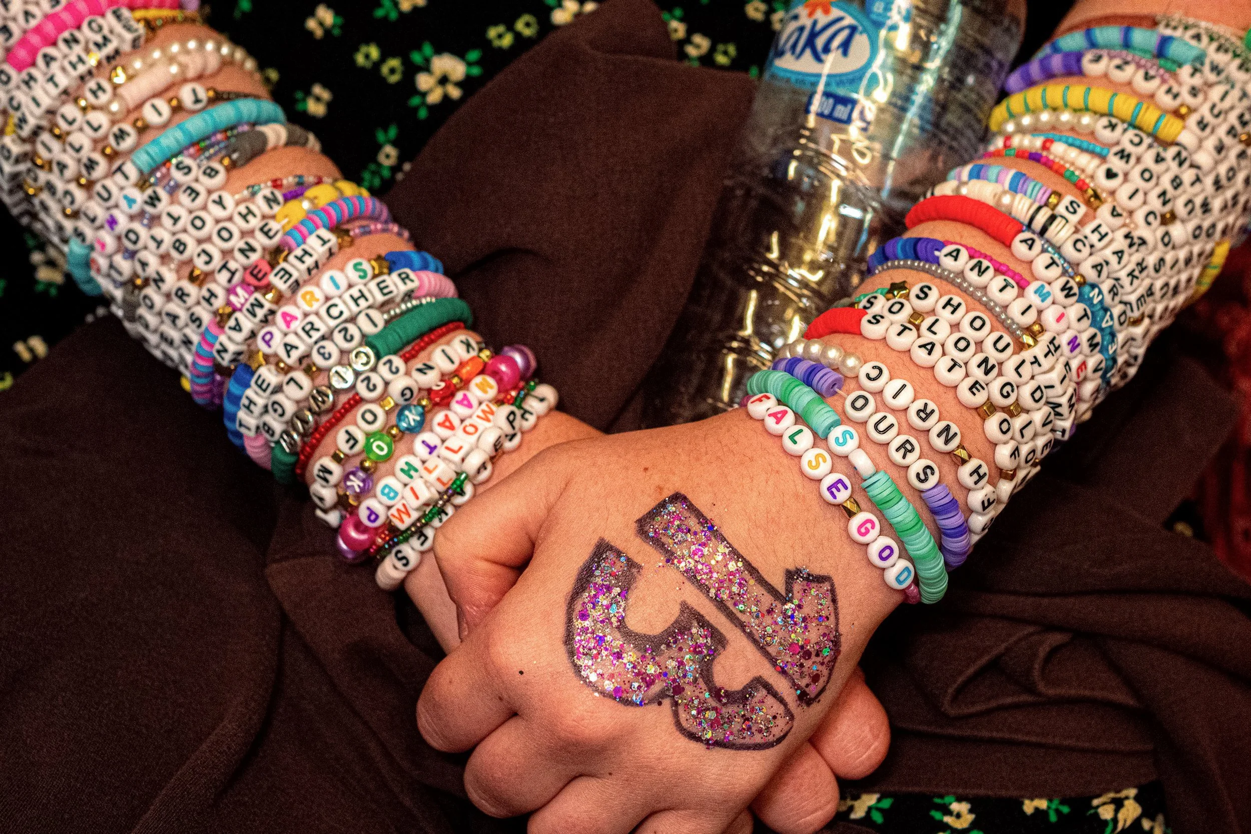 Close-up of a Taylor Swift fan’s crossed hands, stacked friendship bracelets and a glittering number 13 on one hand.