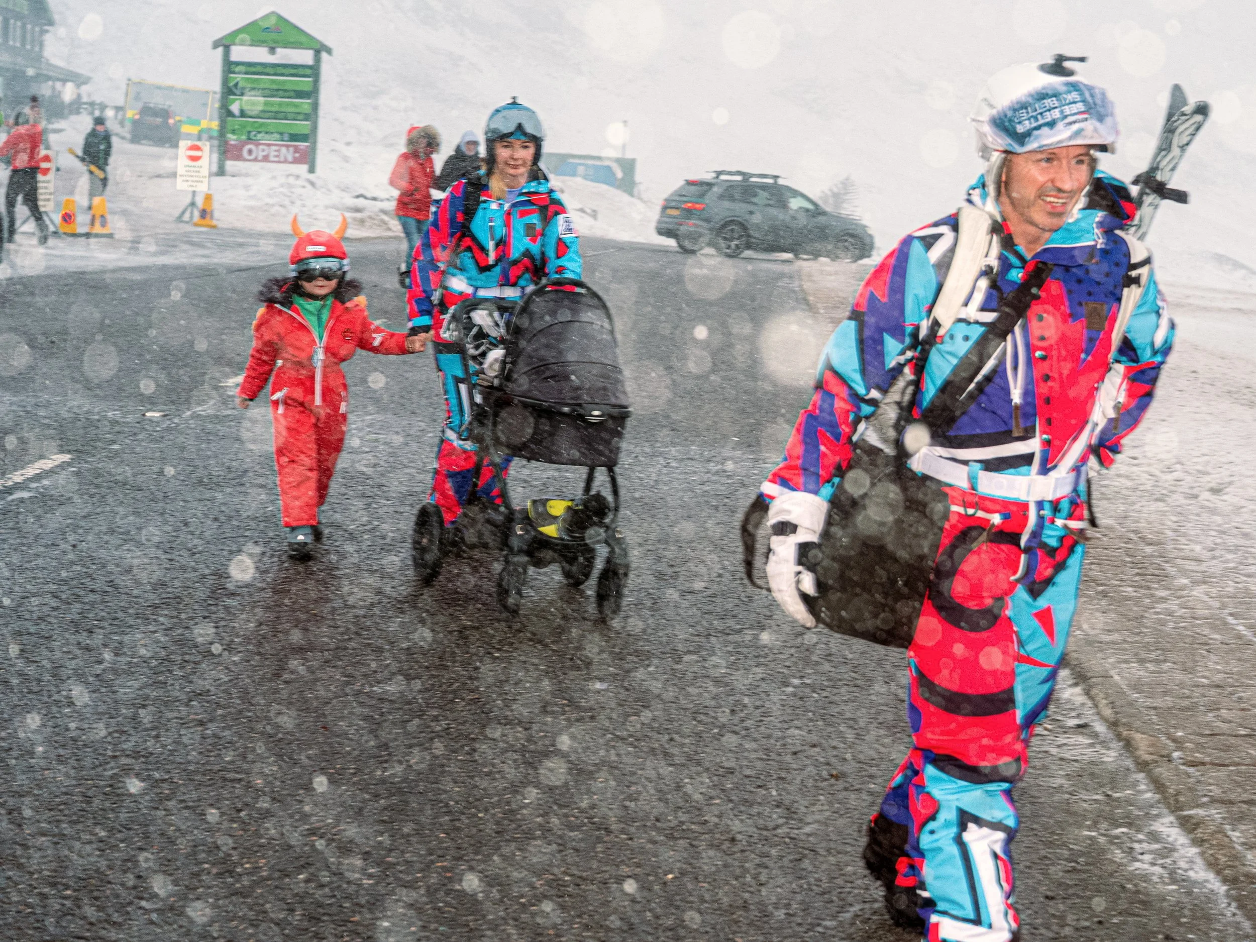 Skiers in bright retro snowsuits walk through snowfall beside a pushchair and a child, from Weather Permitting.