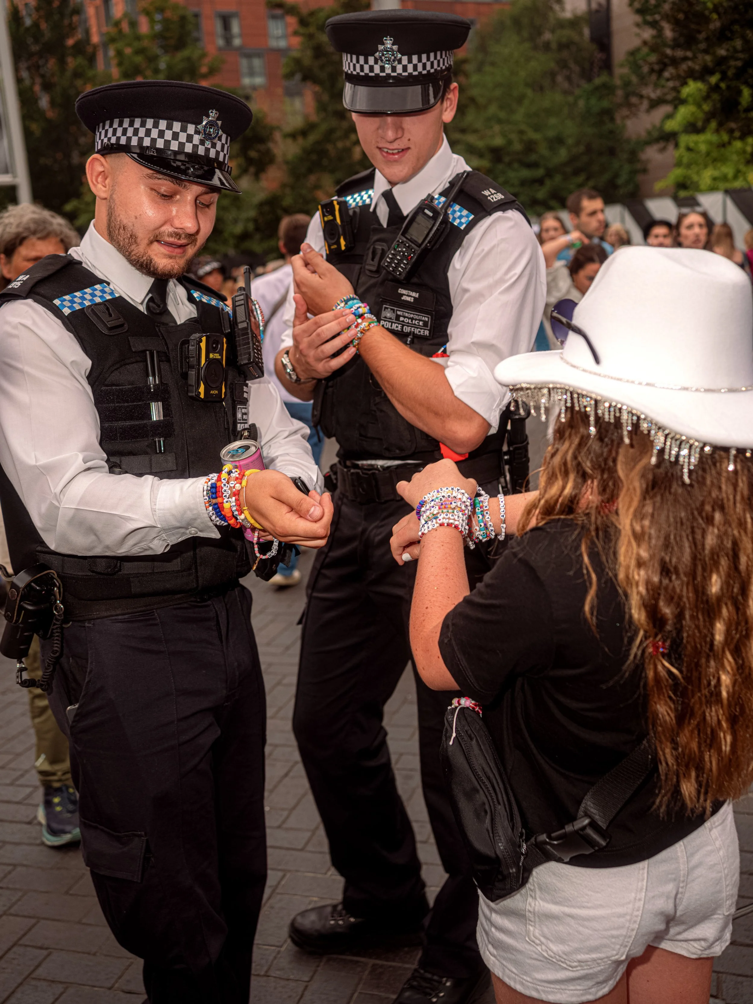 Two police officers hold out their wrists as a young Taylor Swift fan in a white cowboy hat offers friendship bracelets.