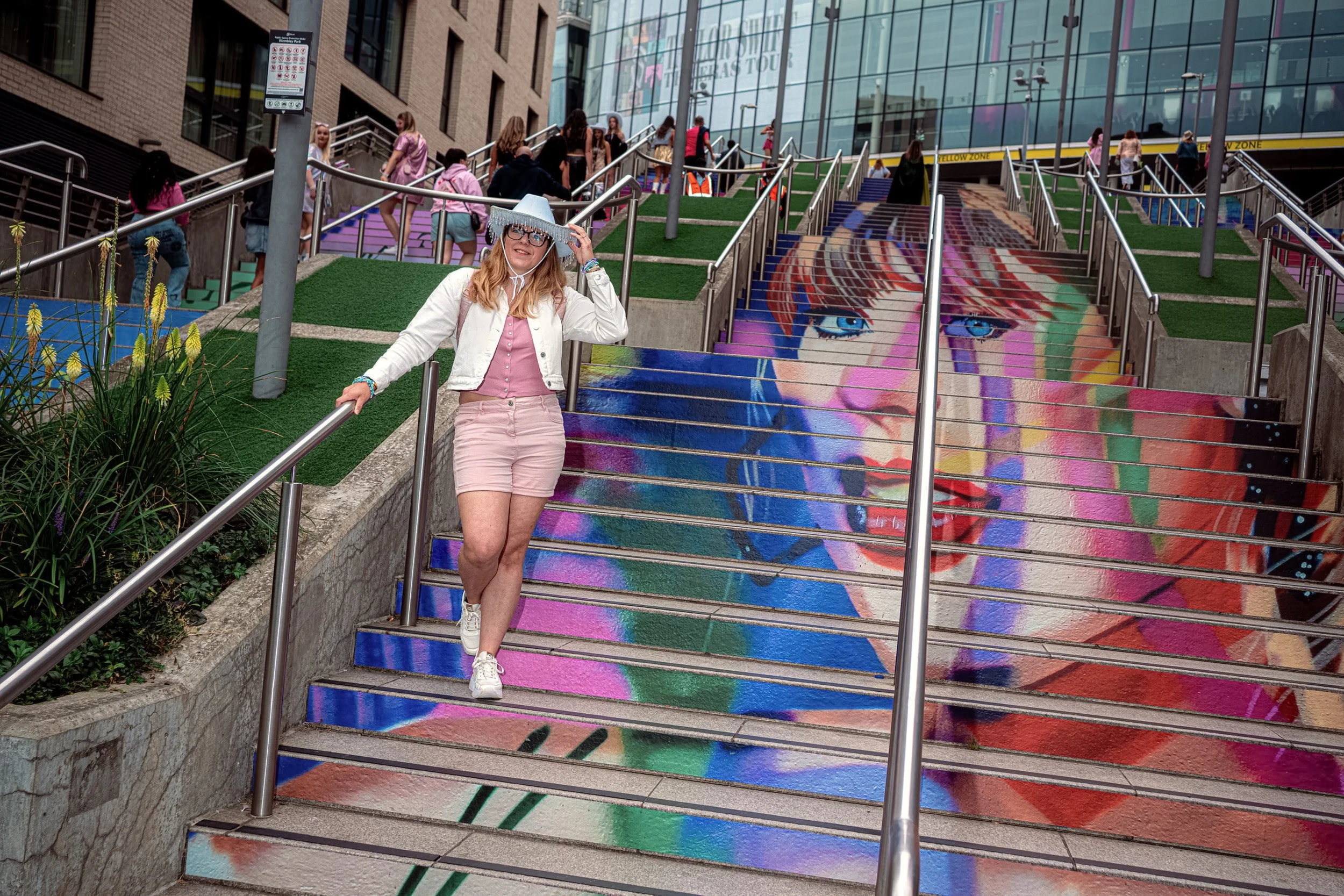 A Taylor Swift fan in a white jacket descends a staircase painted with a large colourful portrait of the singer.