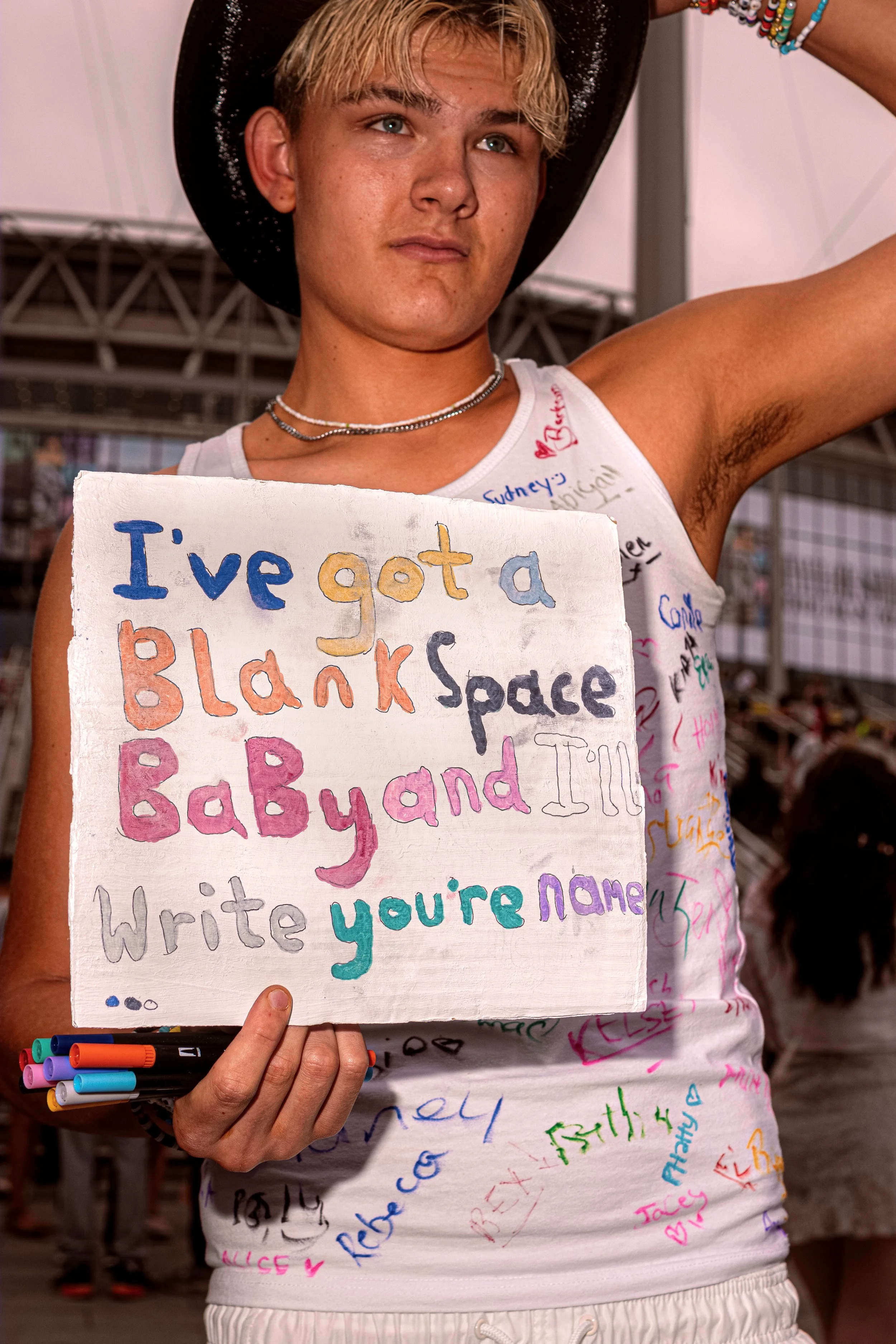 A Taylor Swift fan in a black cowboy hat holds a colourful handwritten sign quoting “Blank Space”.