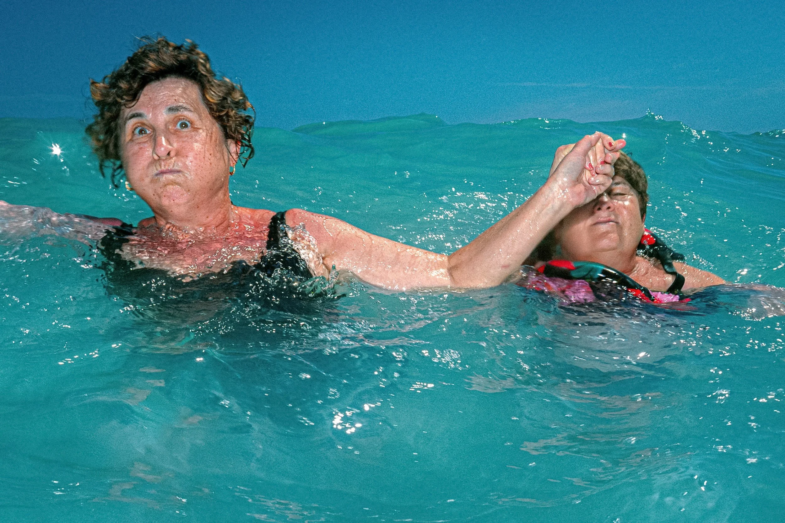 Two swimmers hold hands while treading water in a choppy turquoise sea.