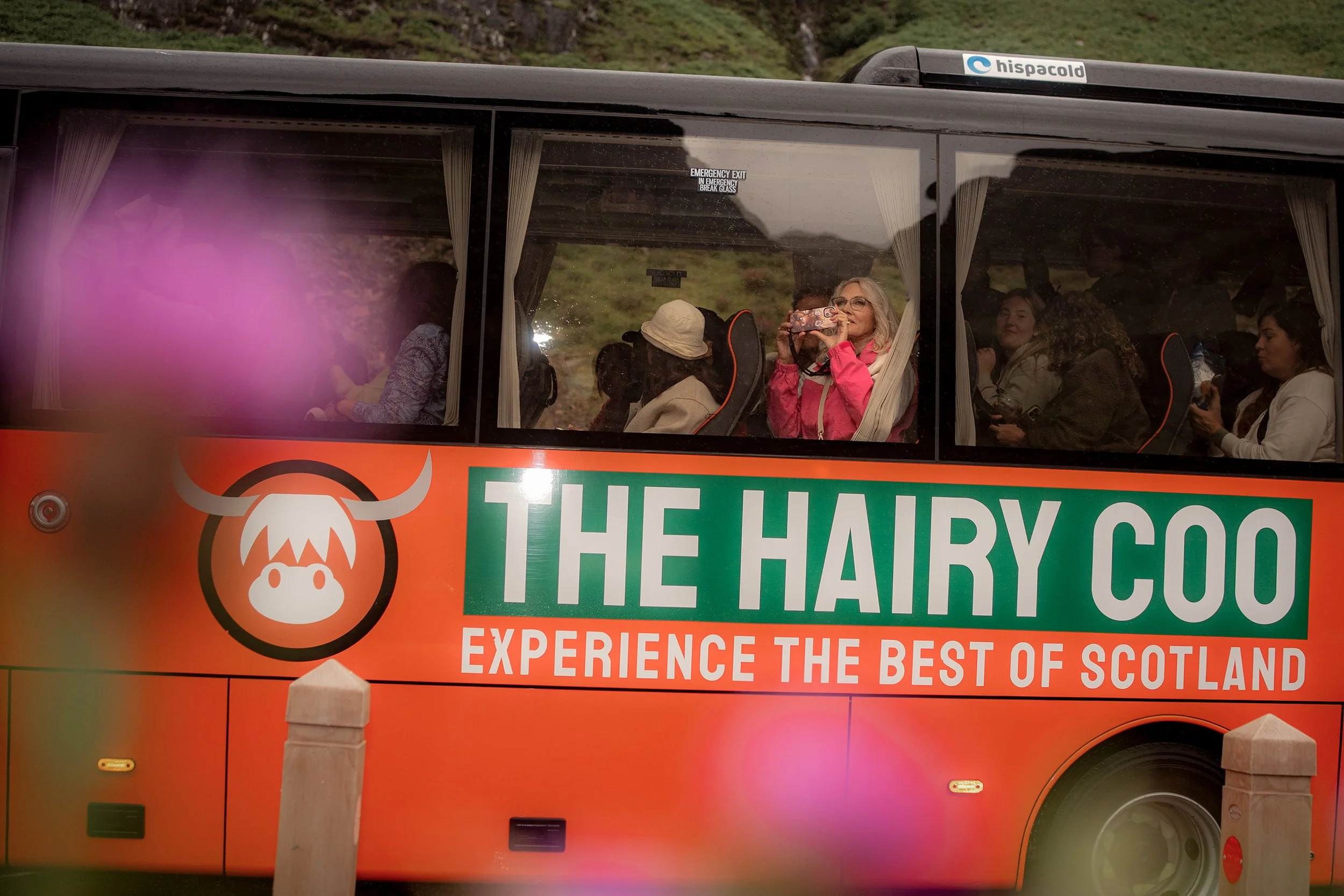 Passengers take photographs through the window of a Hairy Coo tour coach.