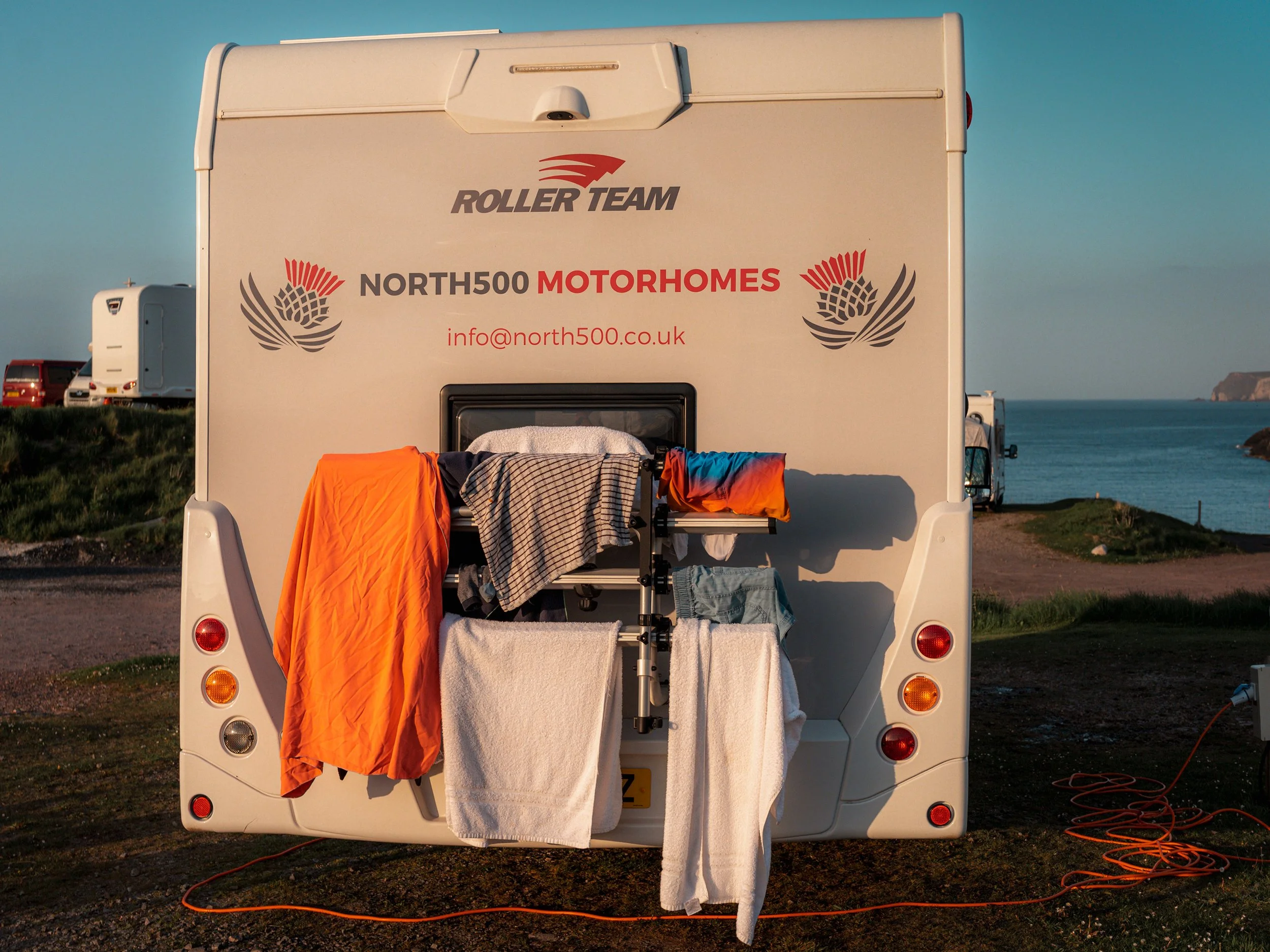 Washing hangs from the back of a North500 Motorhomes rental van by the sea.