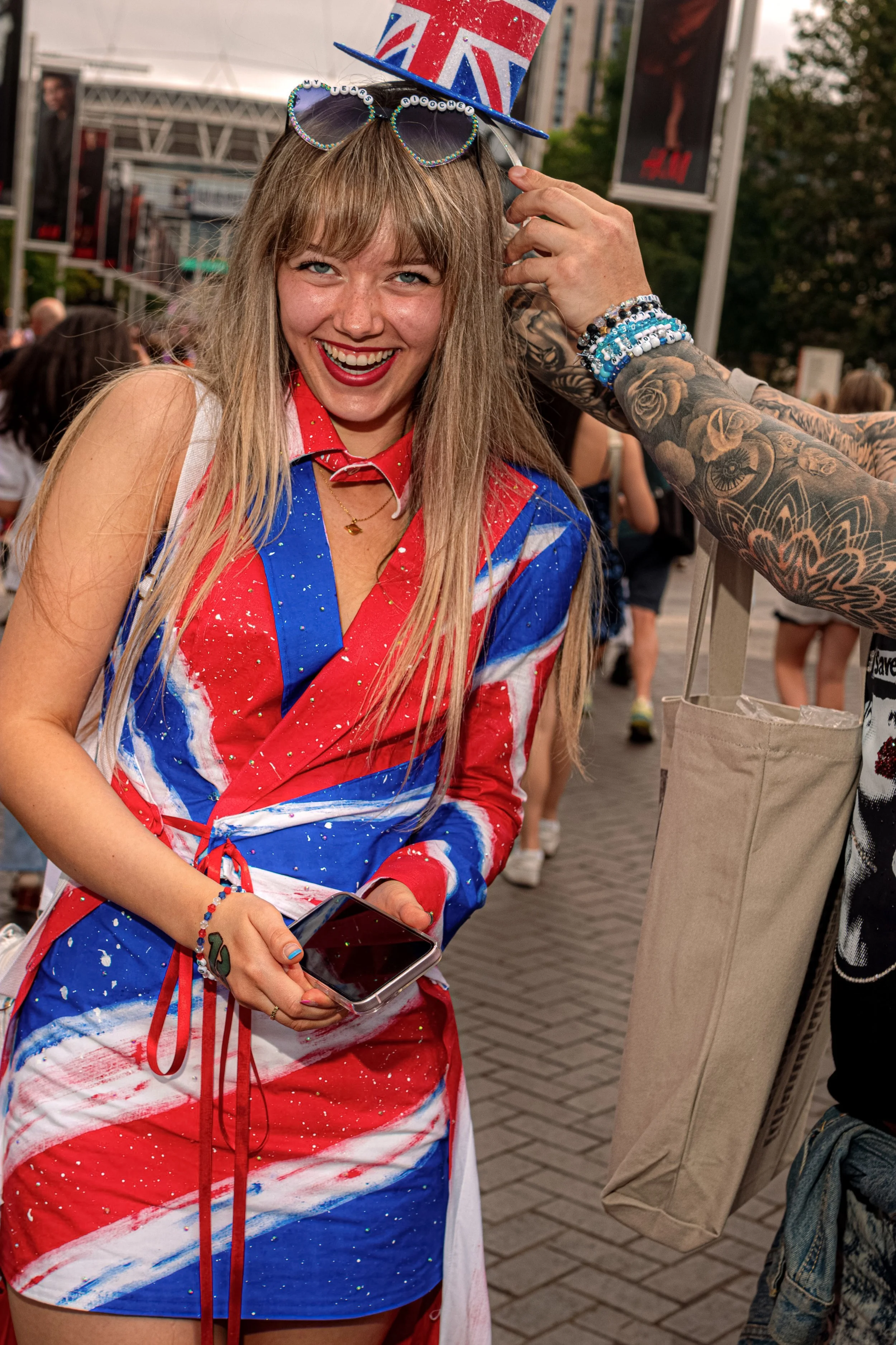 A smiling Taylor Swift fan wears a Union Jack outfit and red heart-shaped sunglasses hanging at her neckline.