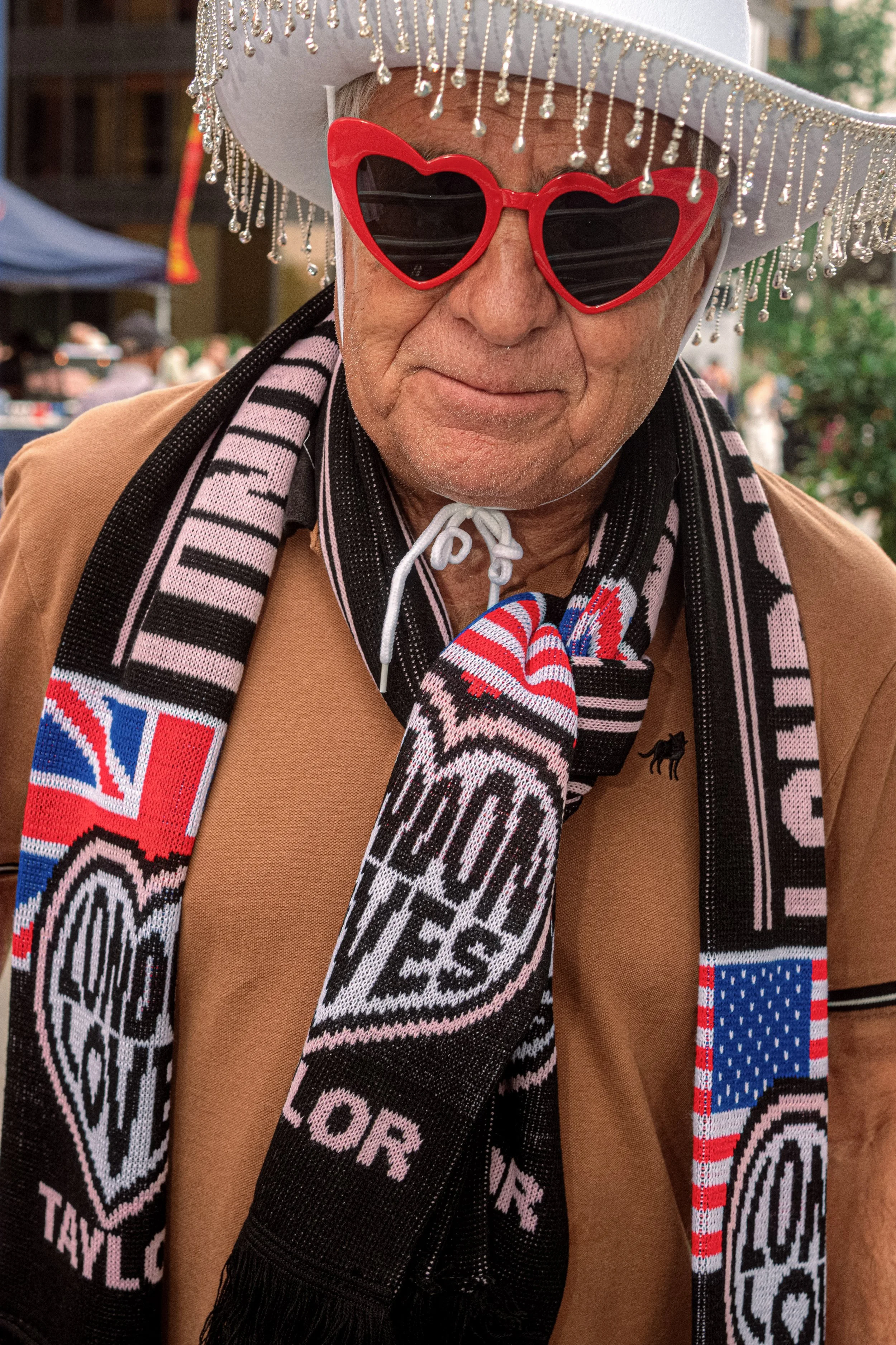 A Taylor Swift fan wears red heart-shaped sunglasses, a silver-fringed cowboy hat and a London Eras Tour scarf.