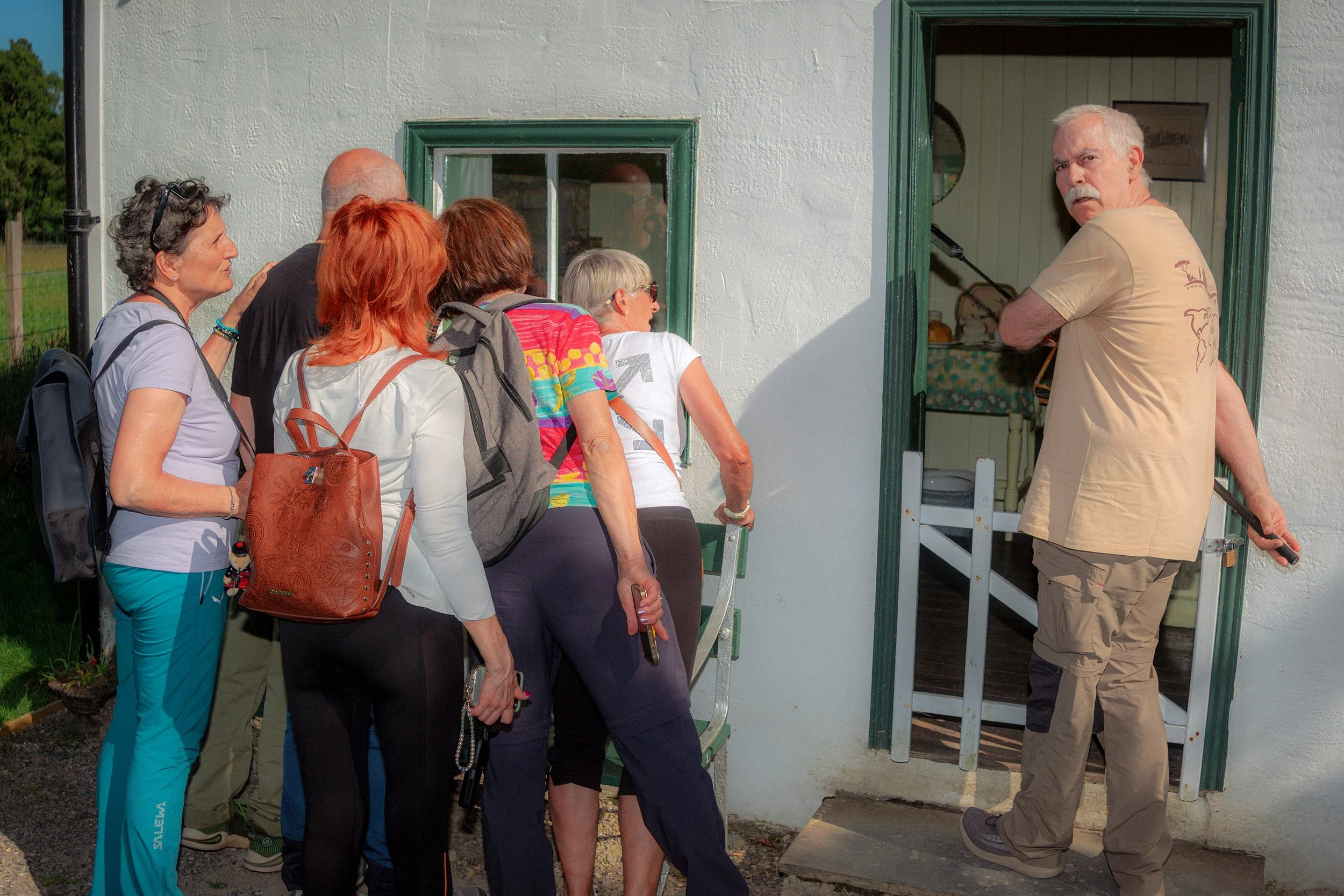 A group of visitors crowds the doorway of a whitewashed cottage as a man looks out.