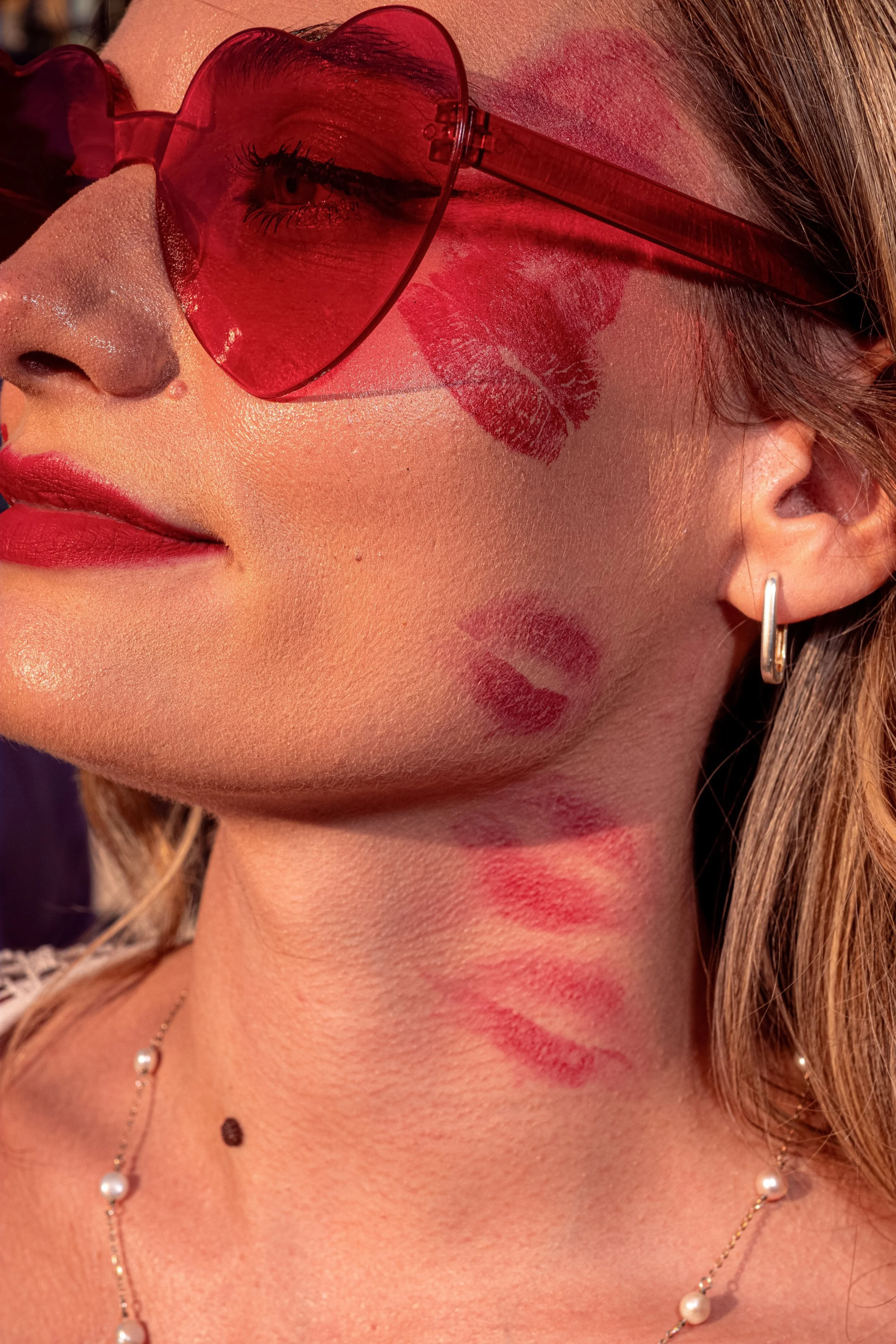 Close-up of a Taylor Swift fan wearing red heart-shaped sunglasses, with lipstick kiss marks on her cheek and neck.