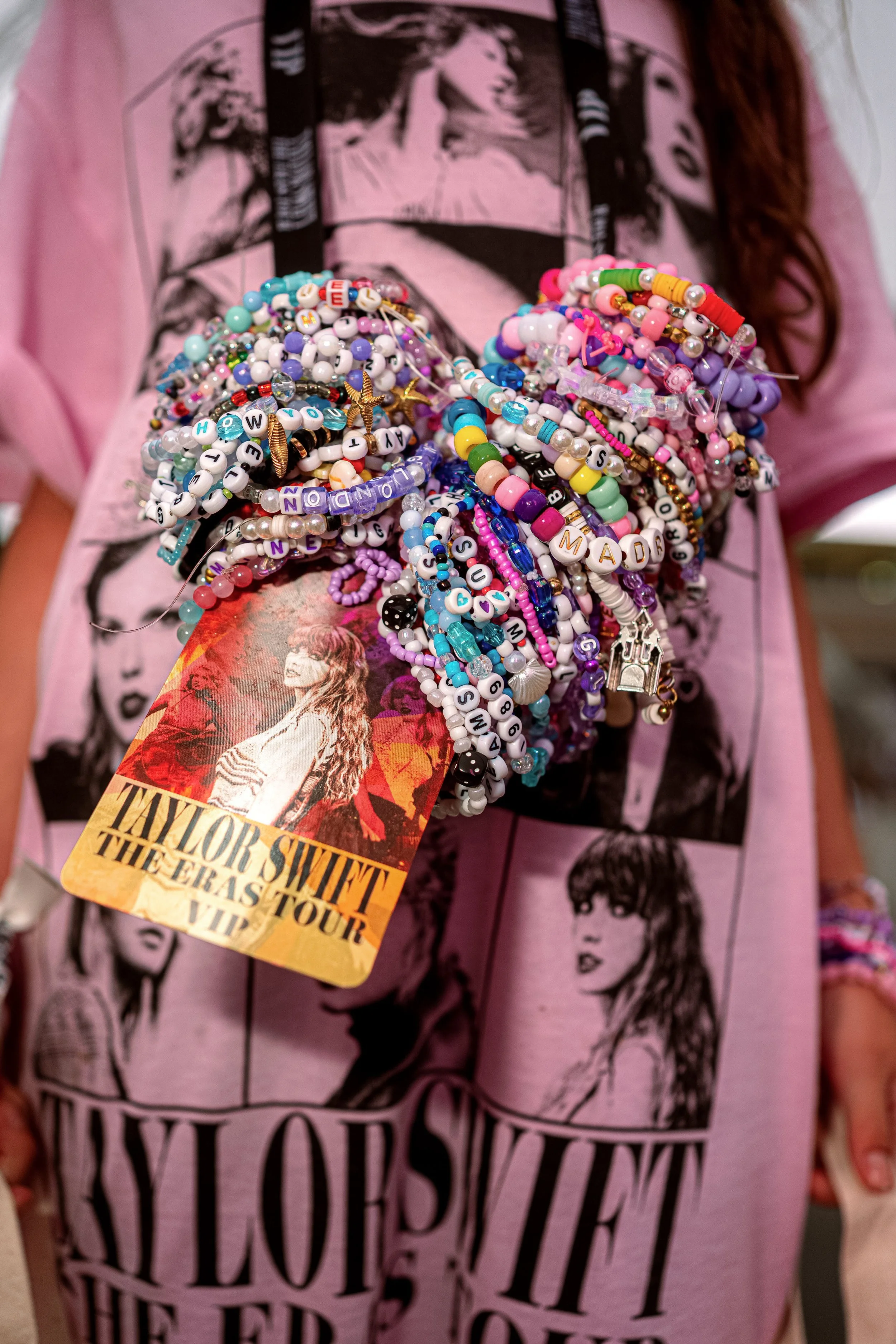 A Taylor Swift fan’s wrist is covered in colourful friendship bracelets beside an Eras Tour lanyard and printed T-shirt.
