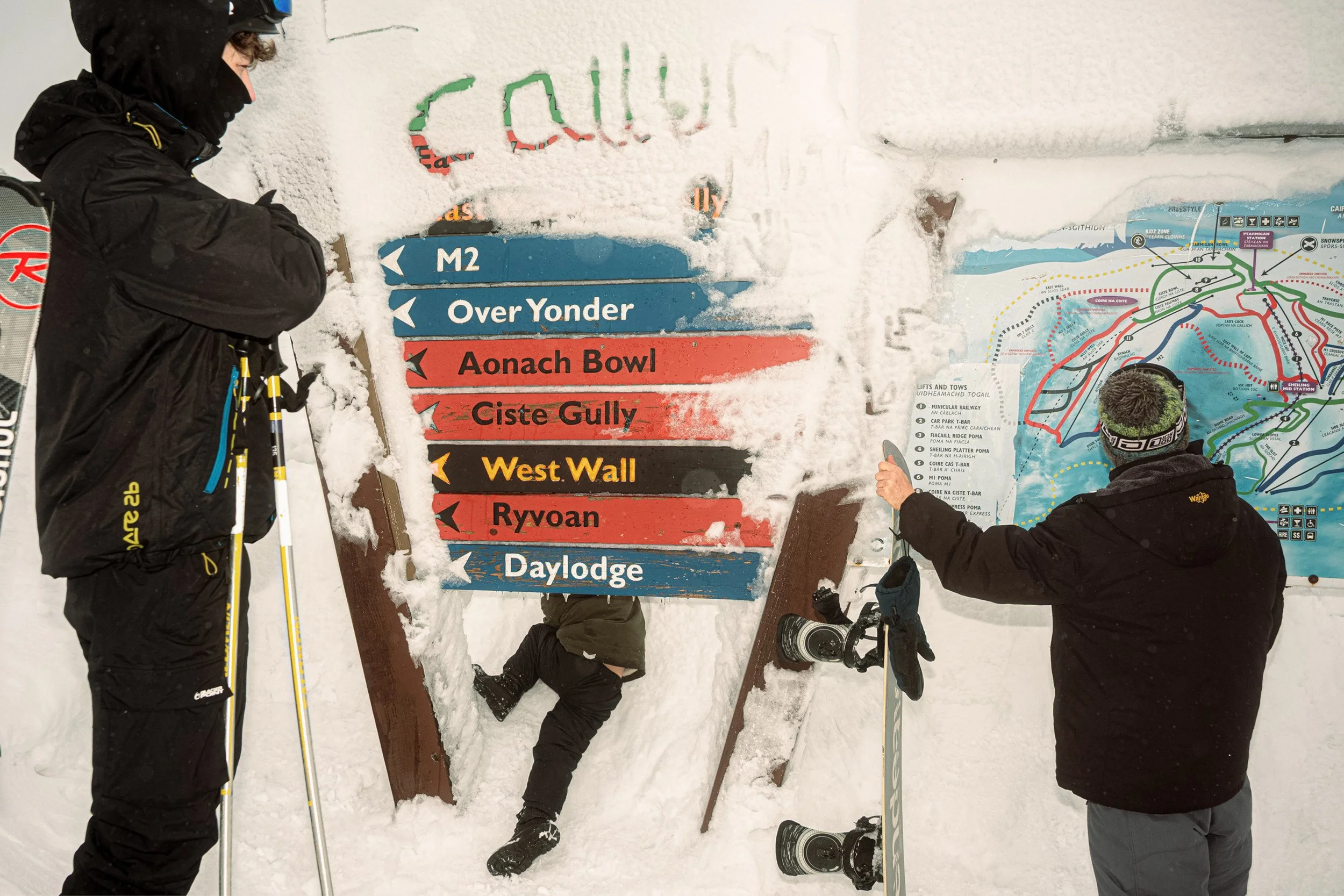 Skiers stand beside snow-covered piste signs and a trail map, from Weather Permitting.