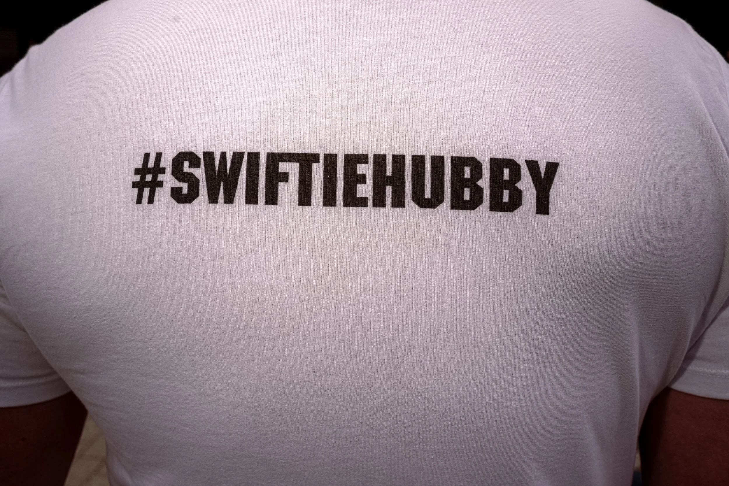 Close-up of a white T-shirt printed with the hashtag “SwiftieHubby”.