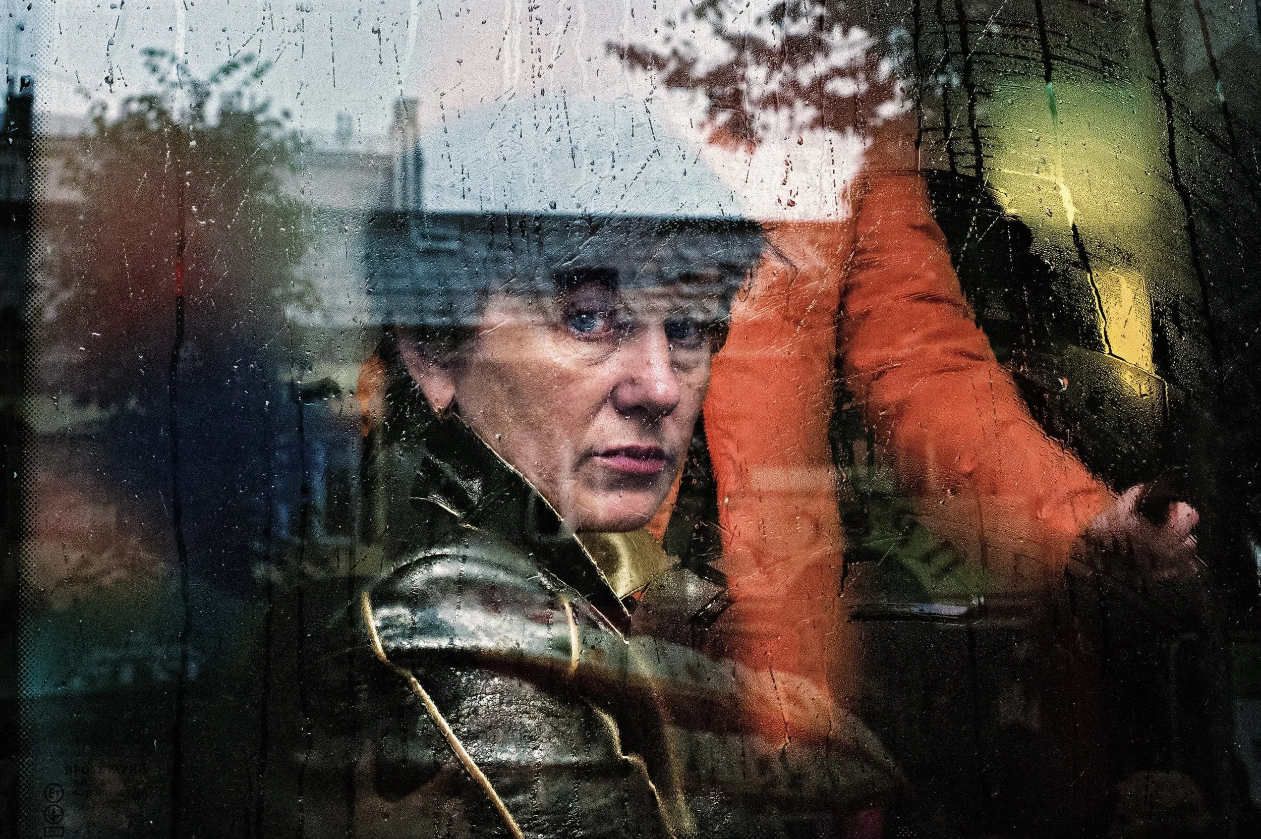 A passenger looks through a rain-streaked bus window layered with reflections.