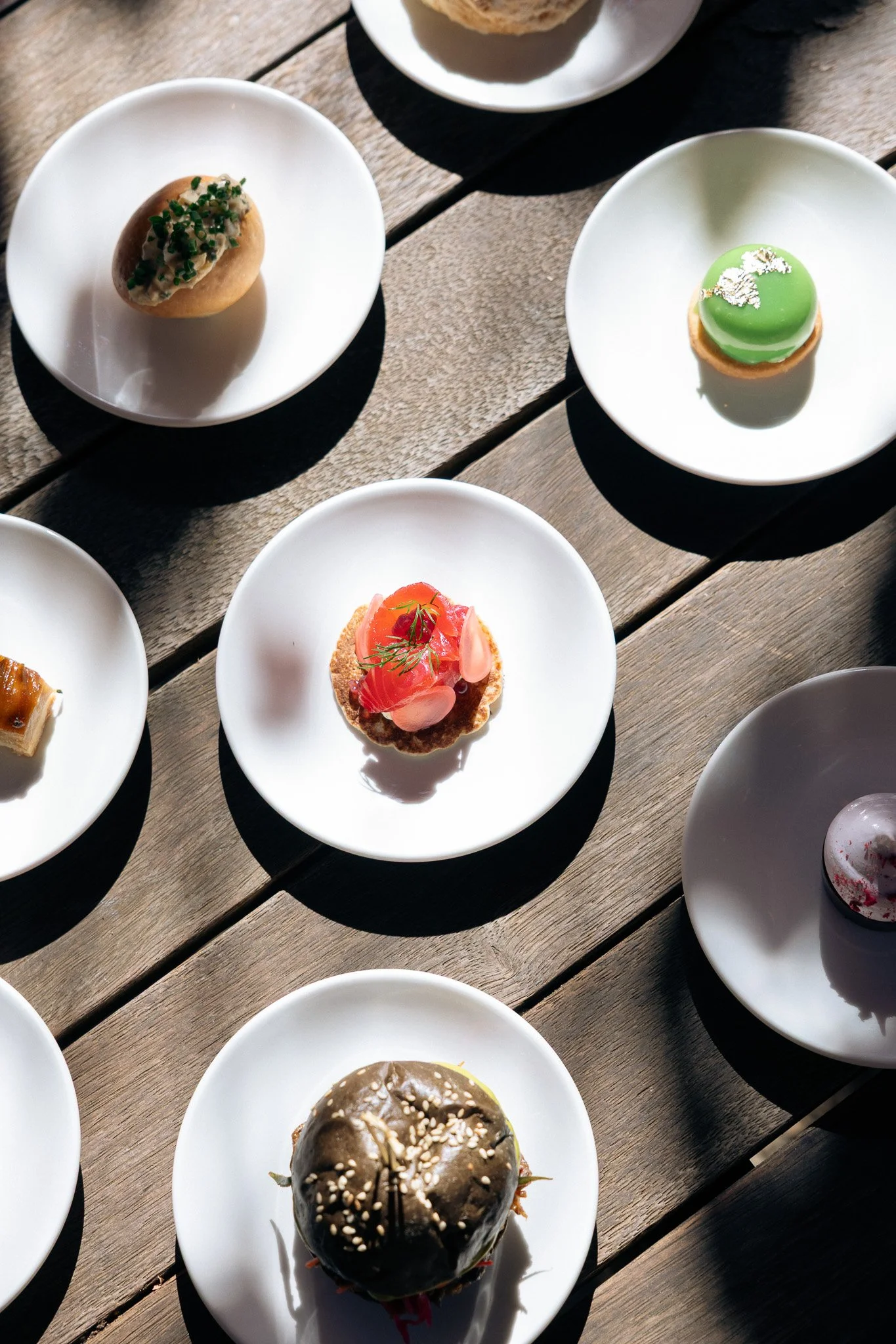 Selection of High Tea items at The Stables at Stones of the Yarra Valley, including savoury bites and refined desserts, each served individually on white plates across a sunlit wooden table.