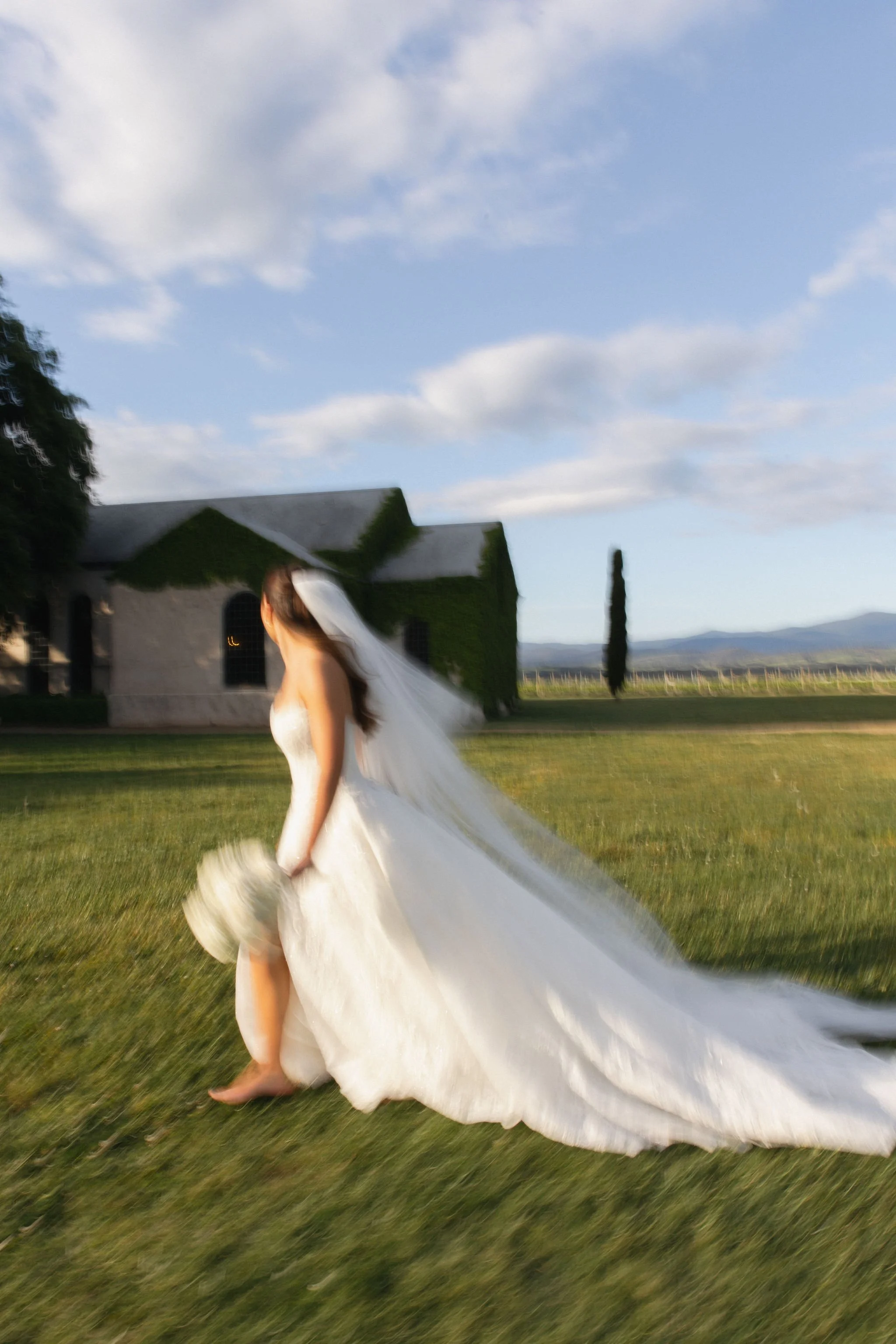 Bride Pippa running across the grounds at Stones of the Yarra Valley with The Chapel in the background, photographed by Ten Acres Agency.