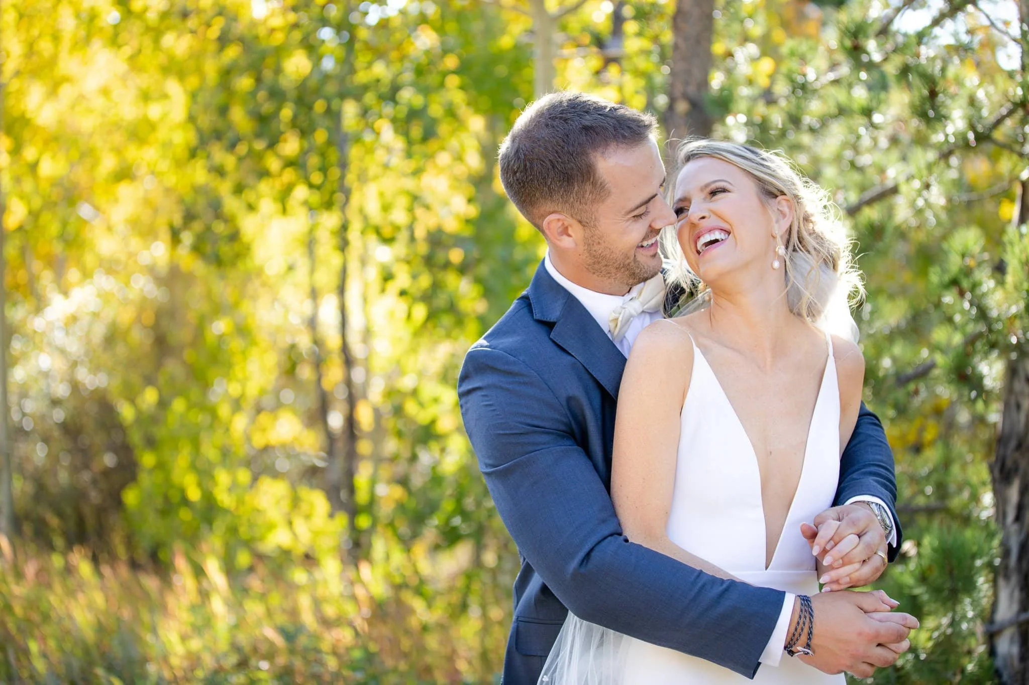 Bride and groom cuddle and laugh in front of yellow aspens