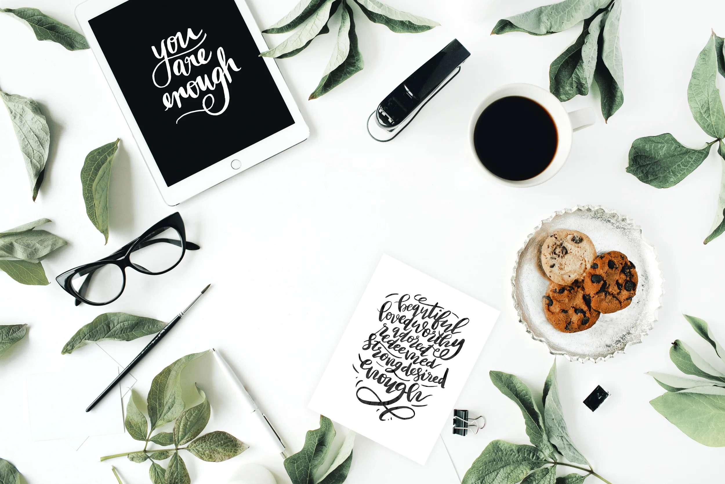 Workspace with tablet, glasses, cup of black coffee, cookies on golden tray, paintbrushes and leaf. Flat lay composition for bloggers, magazines, social media and artists. Top view.