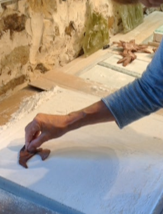 Next the clay forms are pressed into dry plaster which is contained with strips of fiber board on a kiln self.