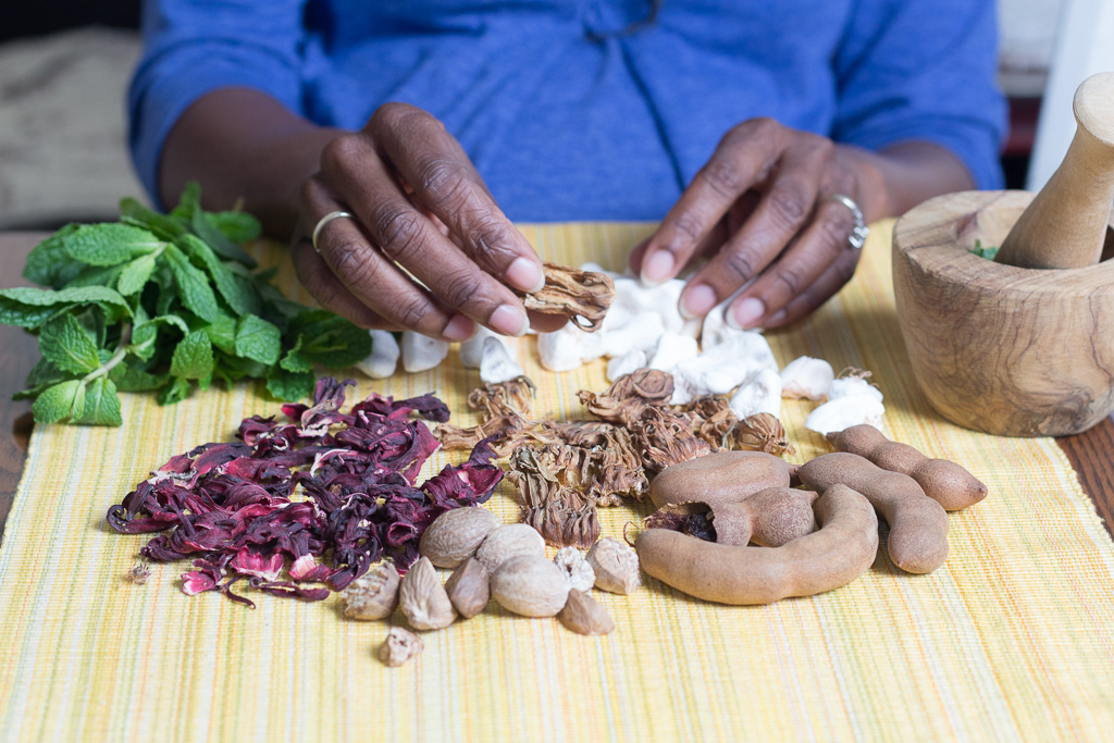 Clockwise from back left: fresh mint, baobab fruit (white pieces), tamarind, dried white hibisicus (in her hand), nutmeg, and dried red hibisicus.