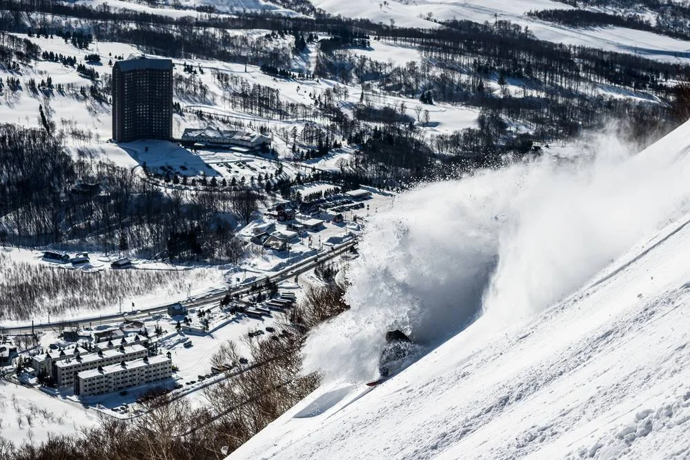 snowboarder throws light snow with Rusutsu filling the background