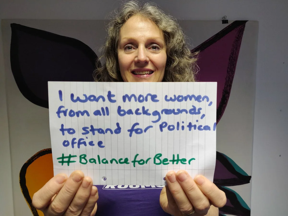 Jane holds a piece of paper which reads “I want more women, from all backgrounds, to stand for political office #BalanceForBetter.”