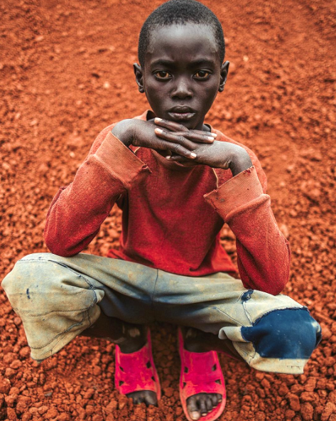 A young boy in Rwanda poses on a pile of dirt.